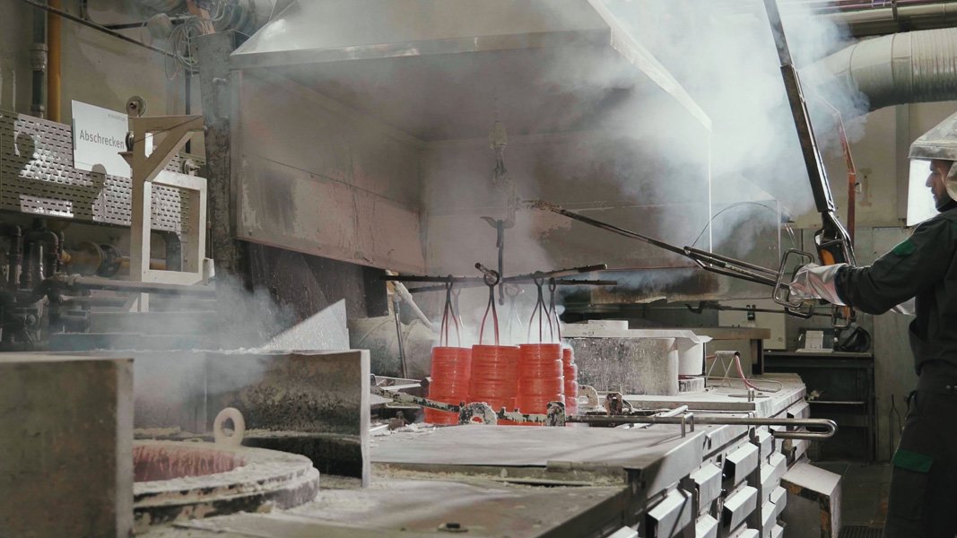 Industriearbeiter beim Abkühlen von Metallformen in einer Fabrikhalle, umgeben von Rauch und technischen Geräten.