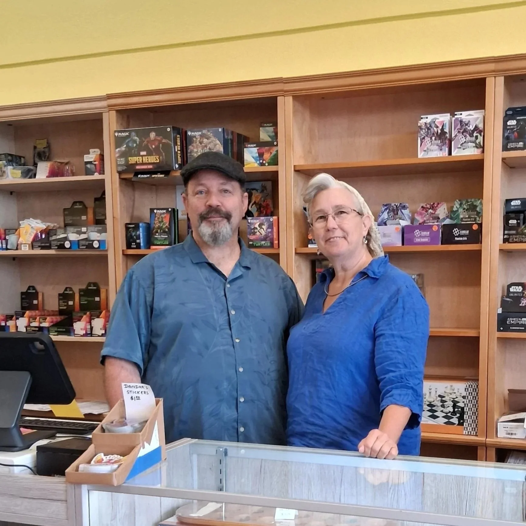 Dan and Doranna "dar" Gilkey, owners.  Middle aged white couple in blue shirts standing in front of shelves of games.