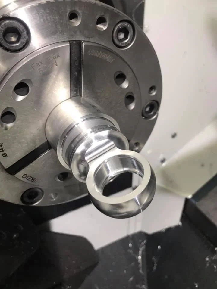 Close-up of a metal machine part with a hollow cylindrical shape mounted on a circular base with multiple bolt holes.