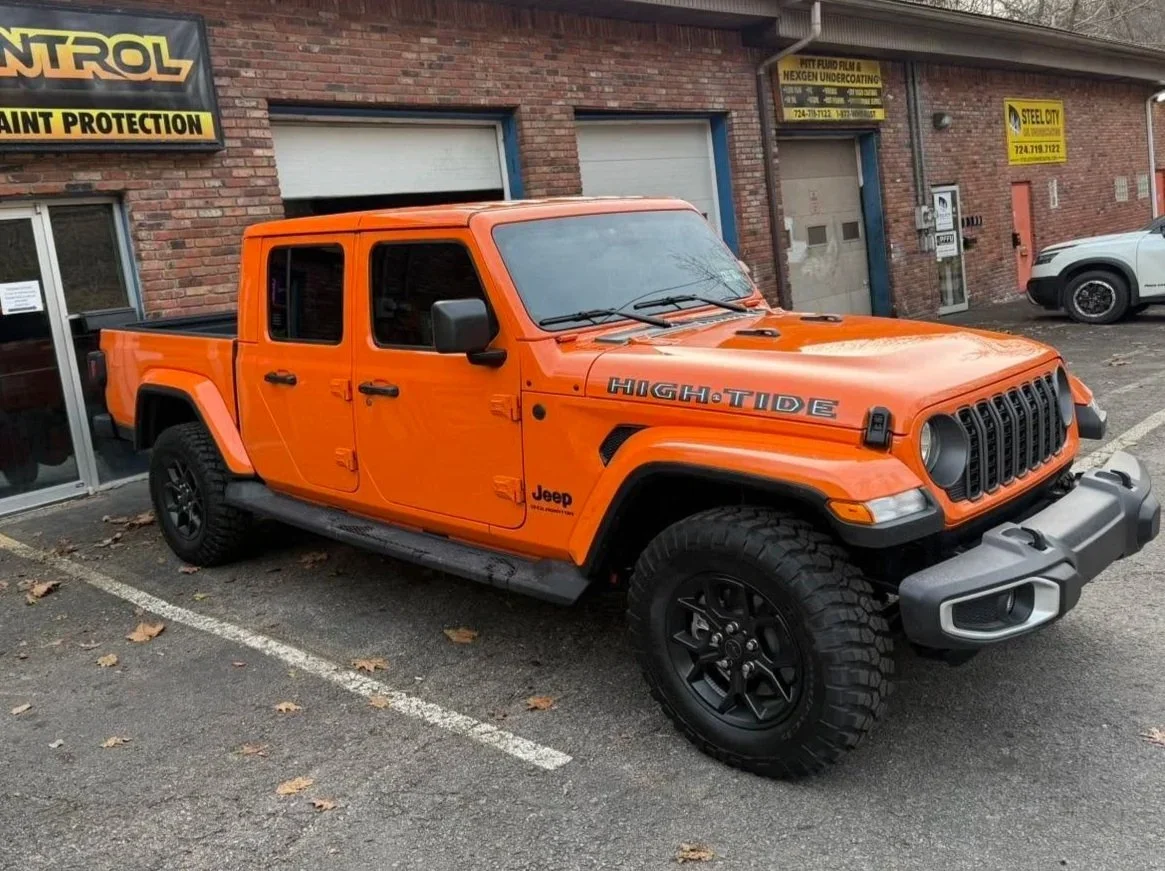 Orange Jeep Gladiator parked in a lot outside a building with signs, including a large high tide decal on the hood.