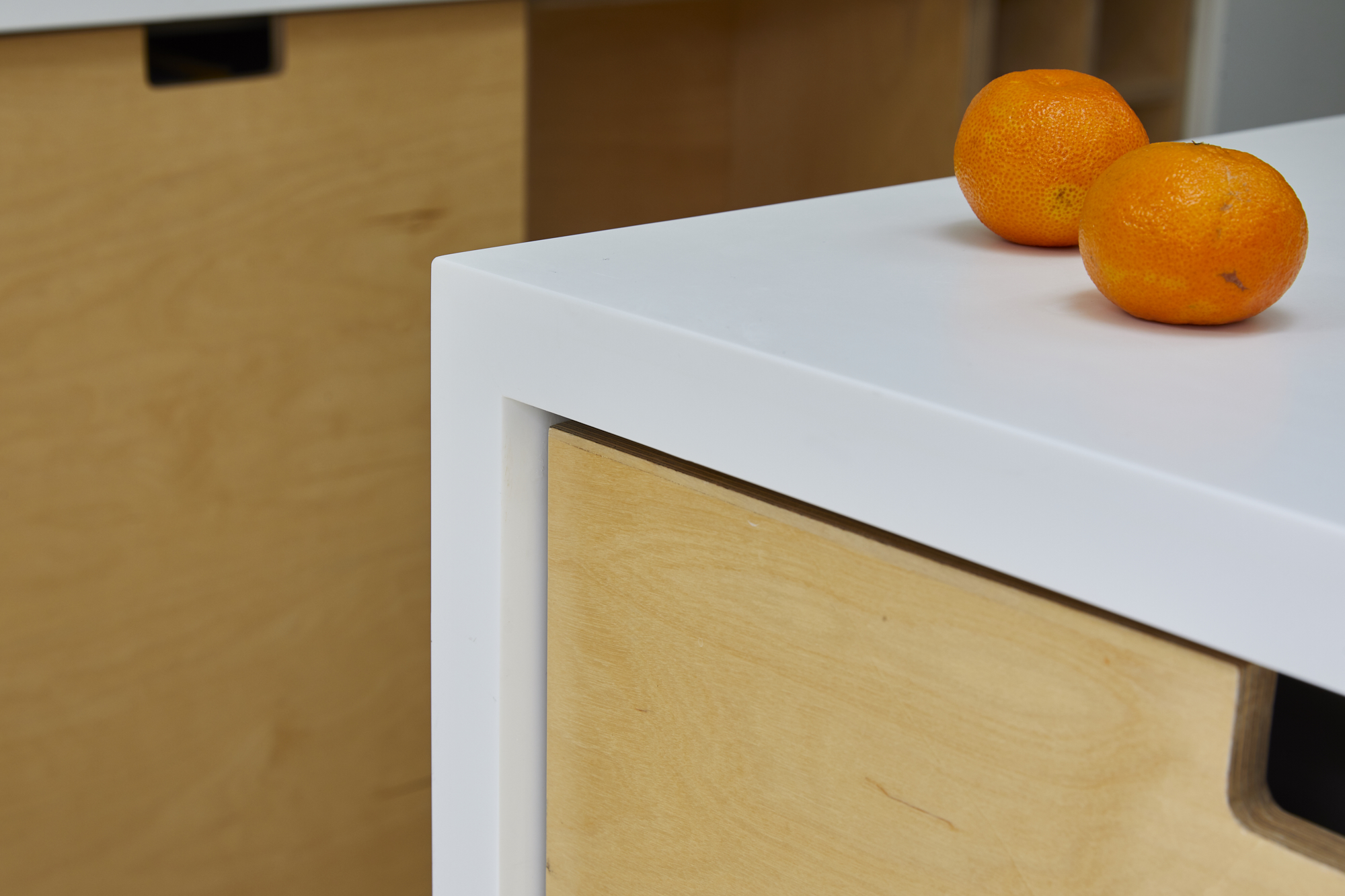 Curated kitchen design in East London - corner view of a white worktop and light wood cabinet door including a tangerine