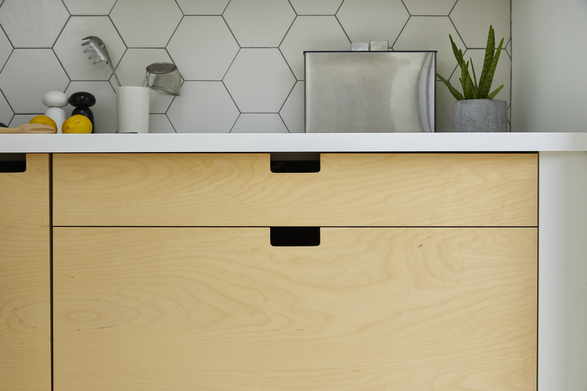 Curated kitchen design in East London - front view of light wood cabinets including geometric tiles, a lemon and a chrome toaster