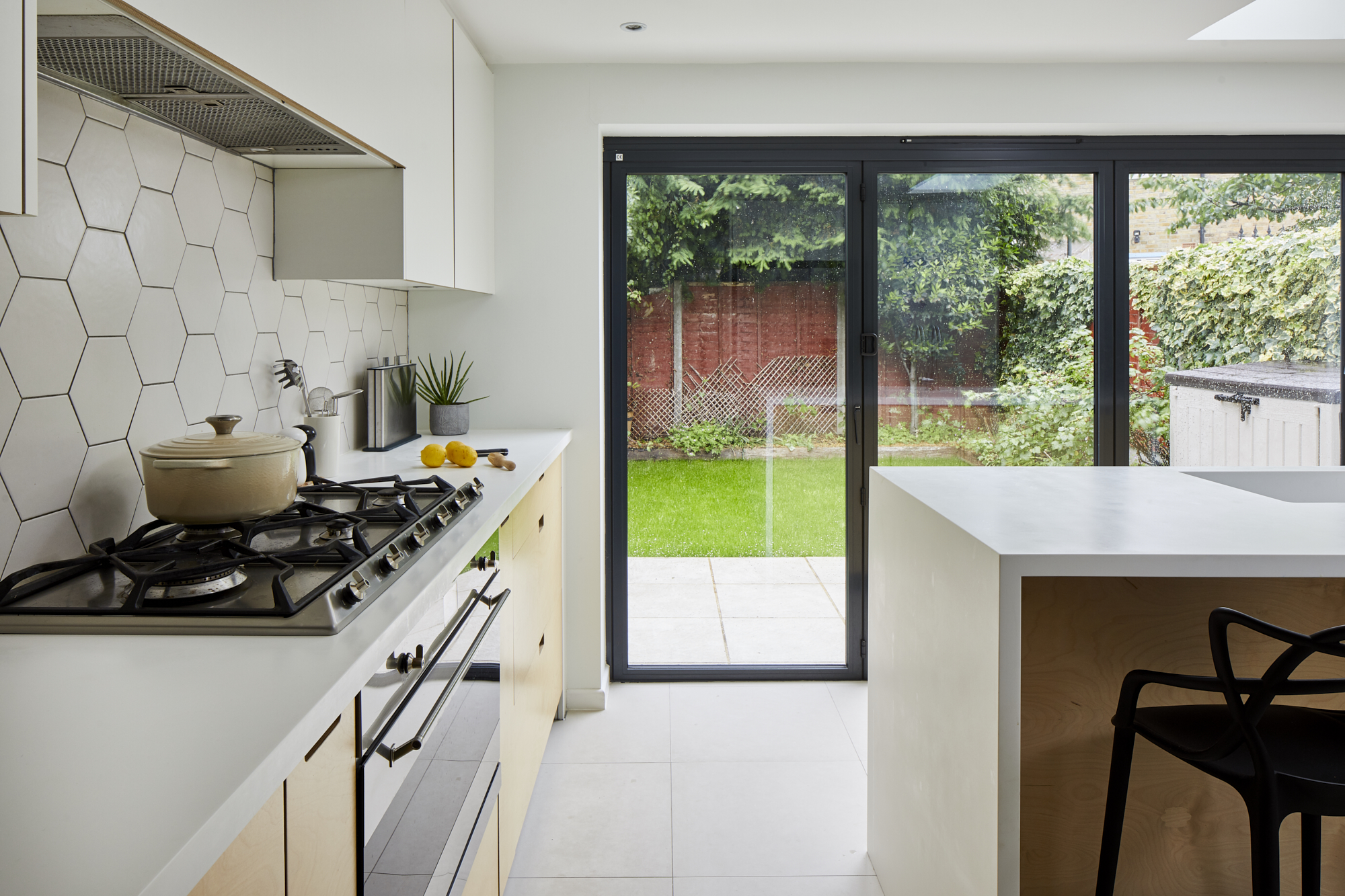 Curated kitchen design in East London - garden view including hob, island and geometric tiles