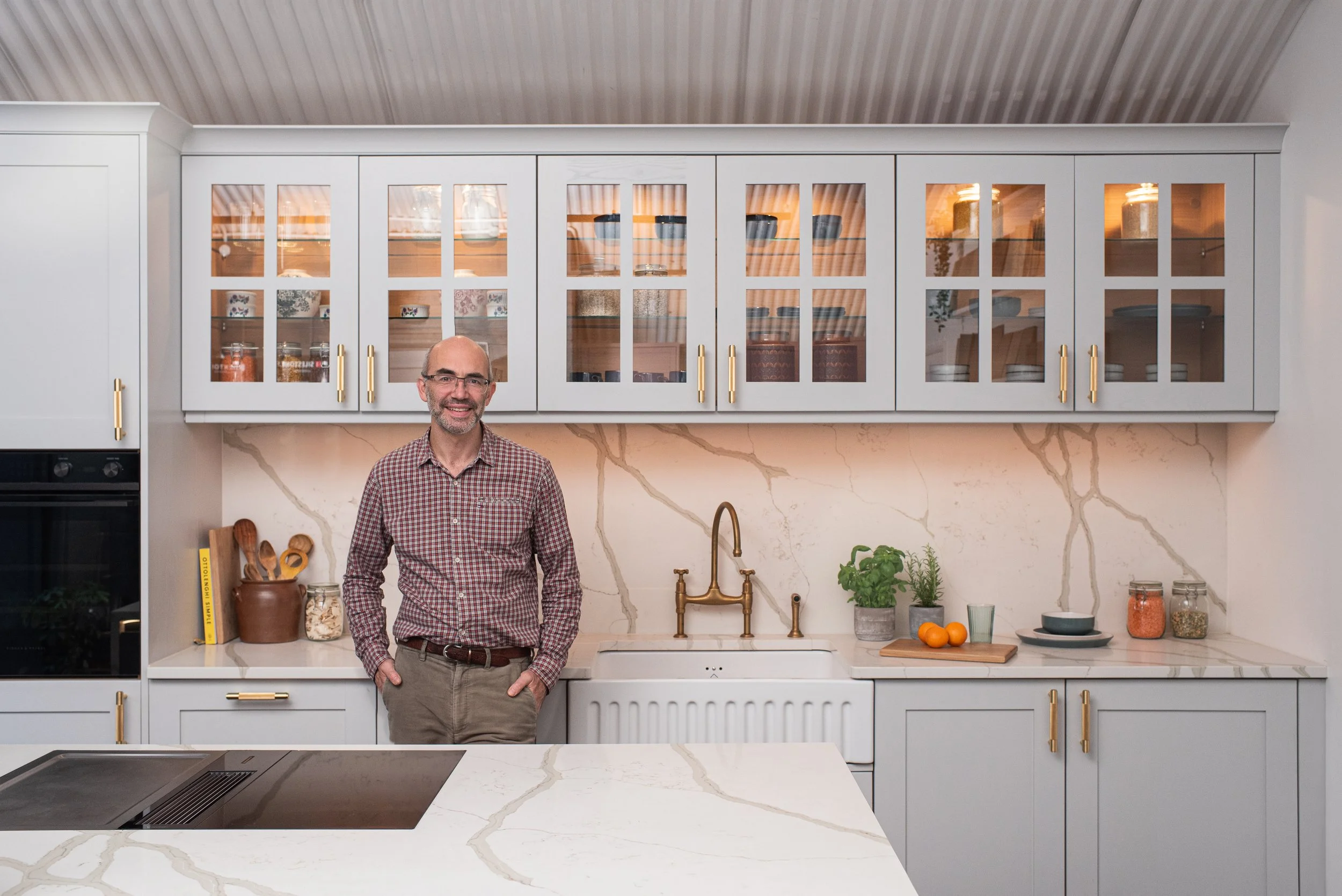 Sebastian from The London Kitchen Company standing in a kitchen with grey cabinetry, brass fittings and a marble-effect island.