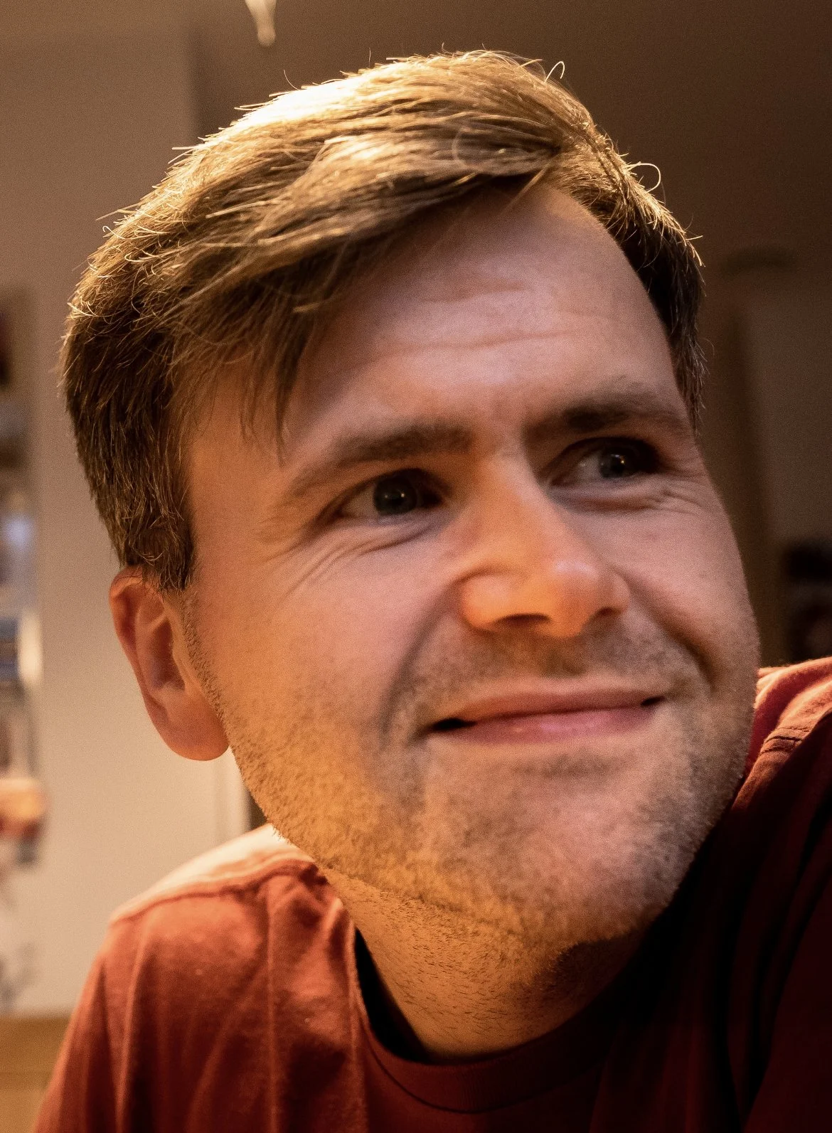 Close-up of Paul Garrity with light brown hair, wearing a reddish-brown shirt, in an indoor setting.