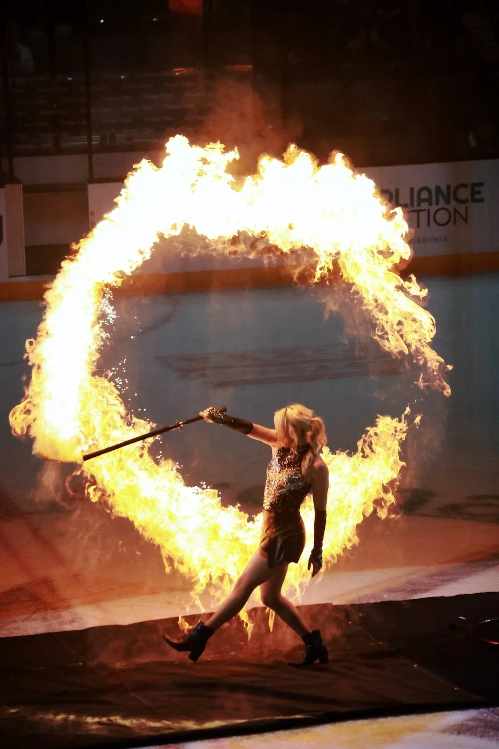 A female fire performer on an ice rink creating a fire halo with a flaming staff.