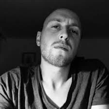 A black-and-white photo of a young man with short hair, looking directly into the camera with a serious expression.