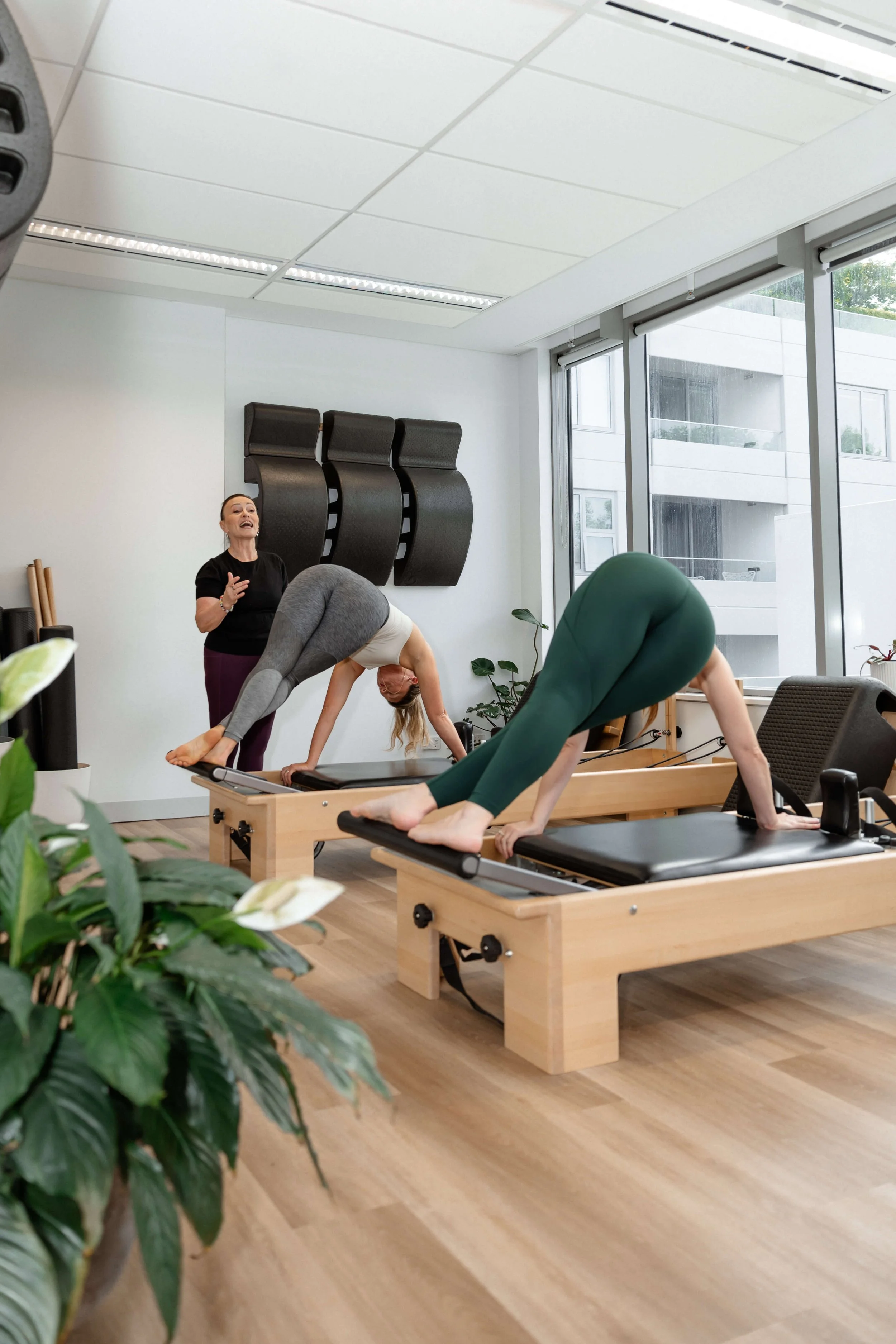 Two women practicing Pilates on reformer machines in a bright, modern studio with an instructor leading the class.