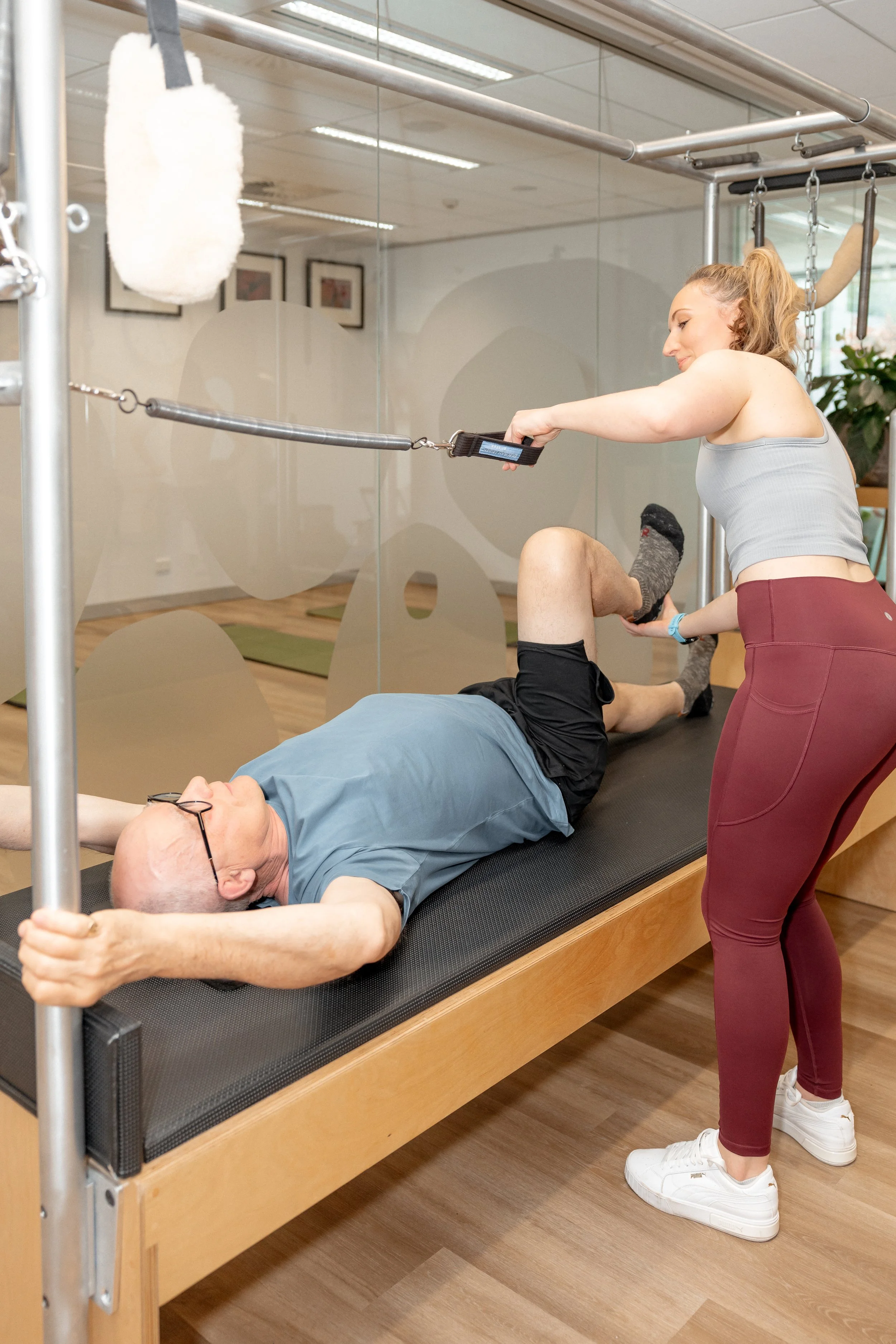 A woman assisting an elderly man with stretching on a therapy table at a fitness center.