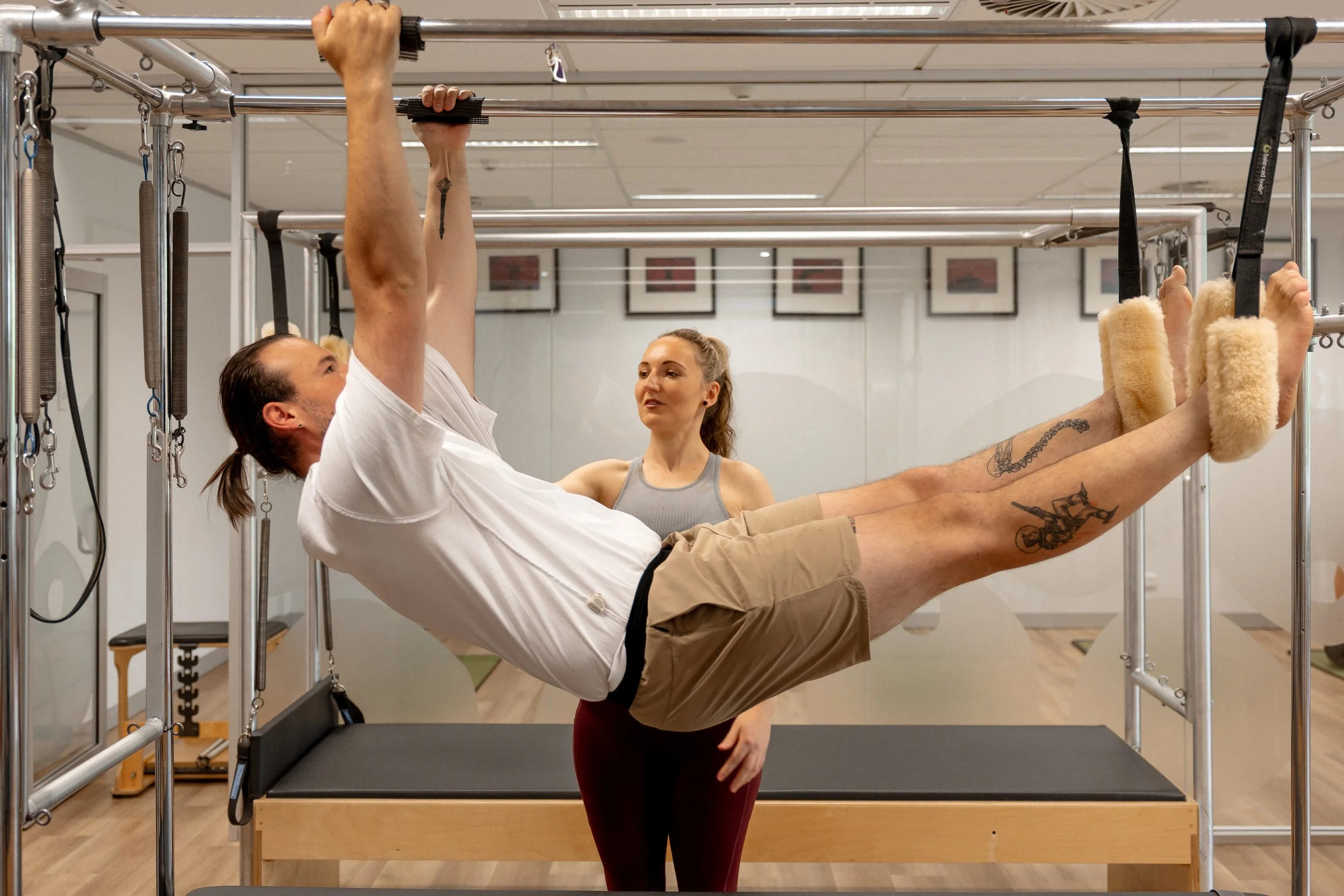 A man doing a wall-supported exercise on a Pilates or rehabilitation frame while a woman observes.