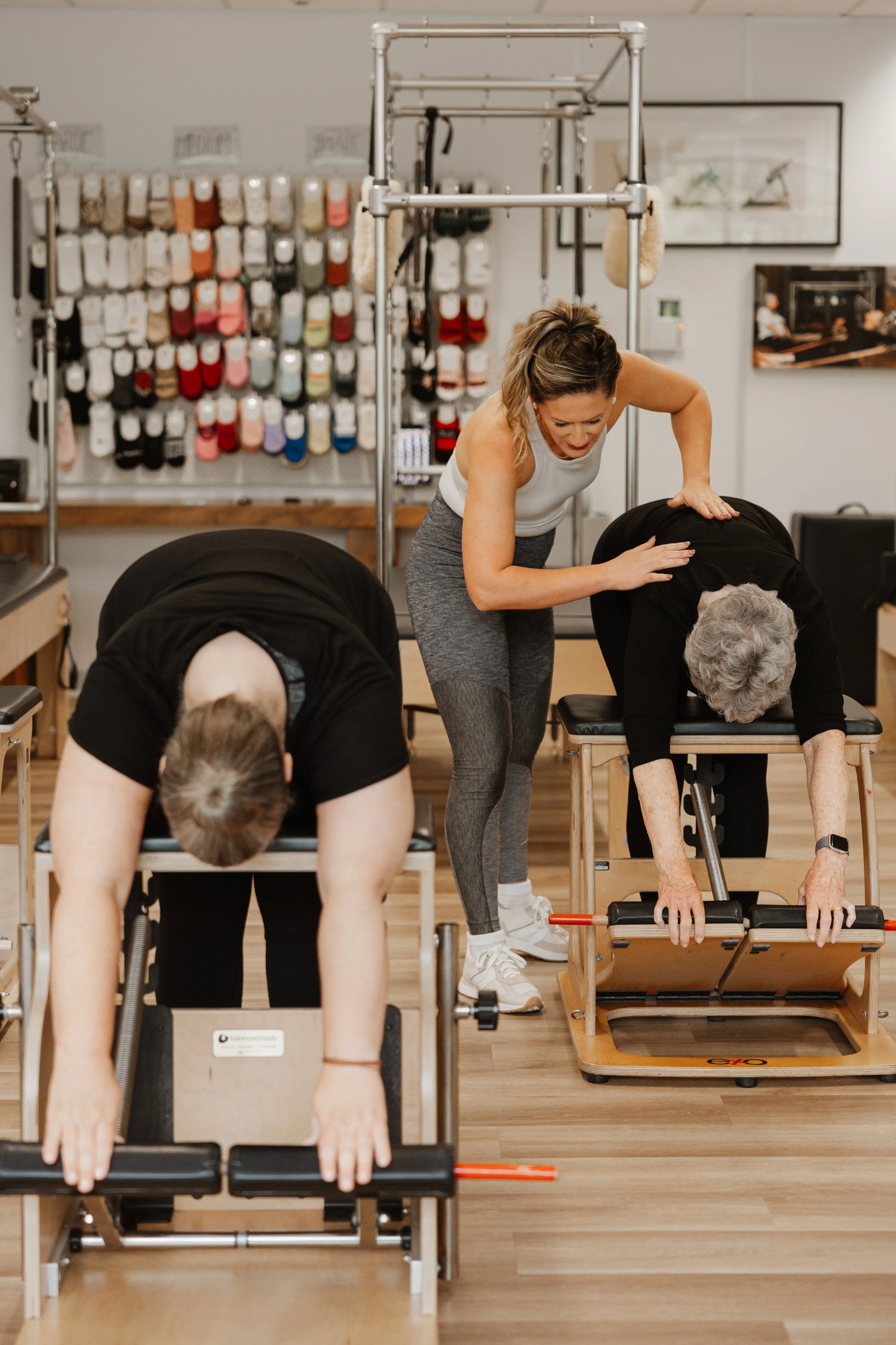 A physical therapy session with a therapist assisting two elderly women in stretching exercises on specialized tables in a therapy clinic.