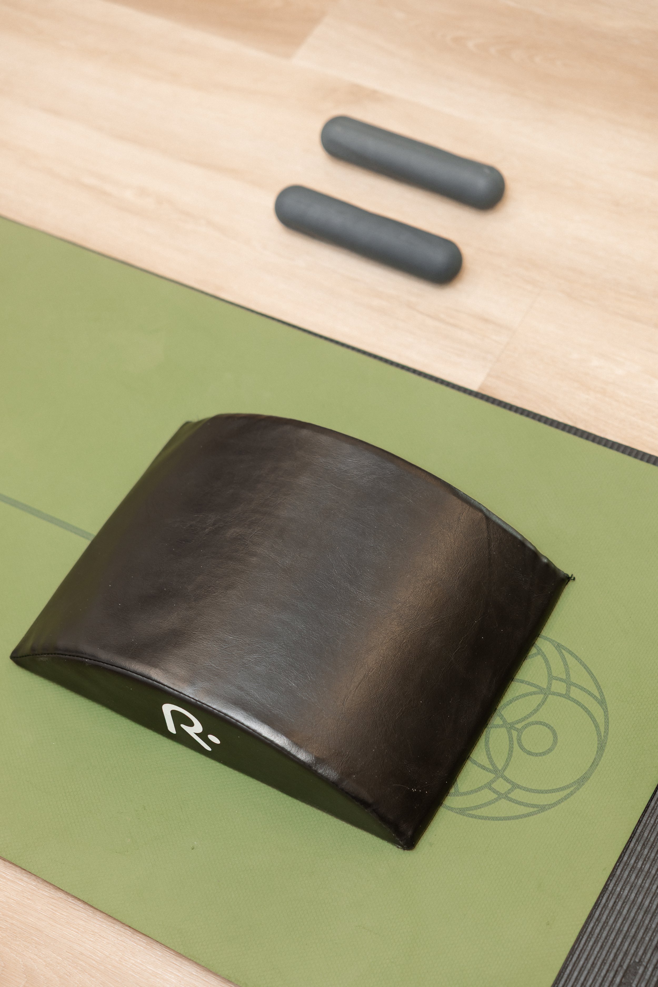A black Pilates box on a green exercise mat next to a wooden table with two small black weights.