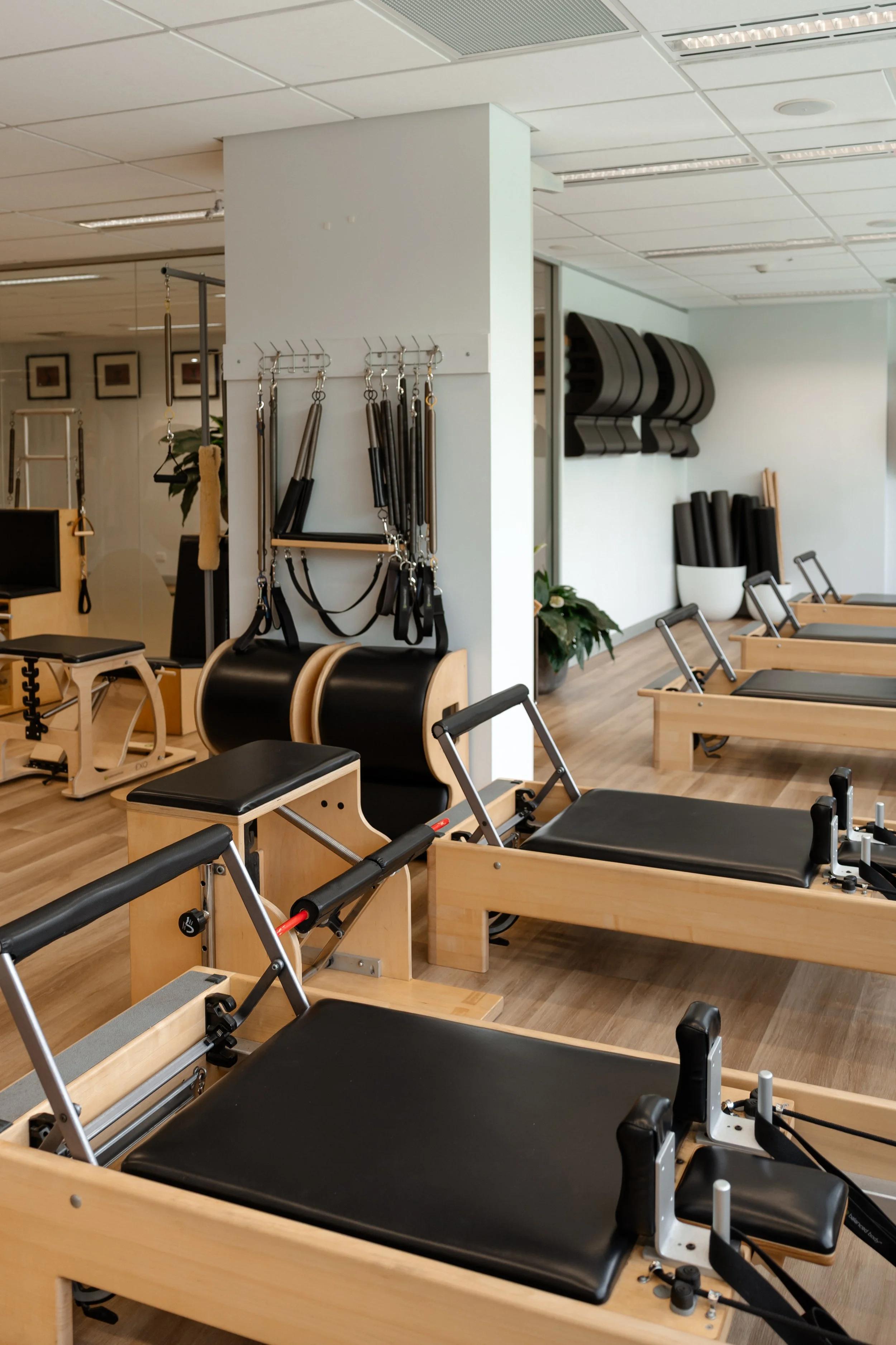 Pilates studio with multiple reformer machines, yoga mats, and fitness equipment arranged in a bright, clean space.
