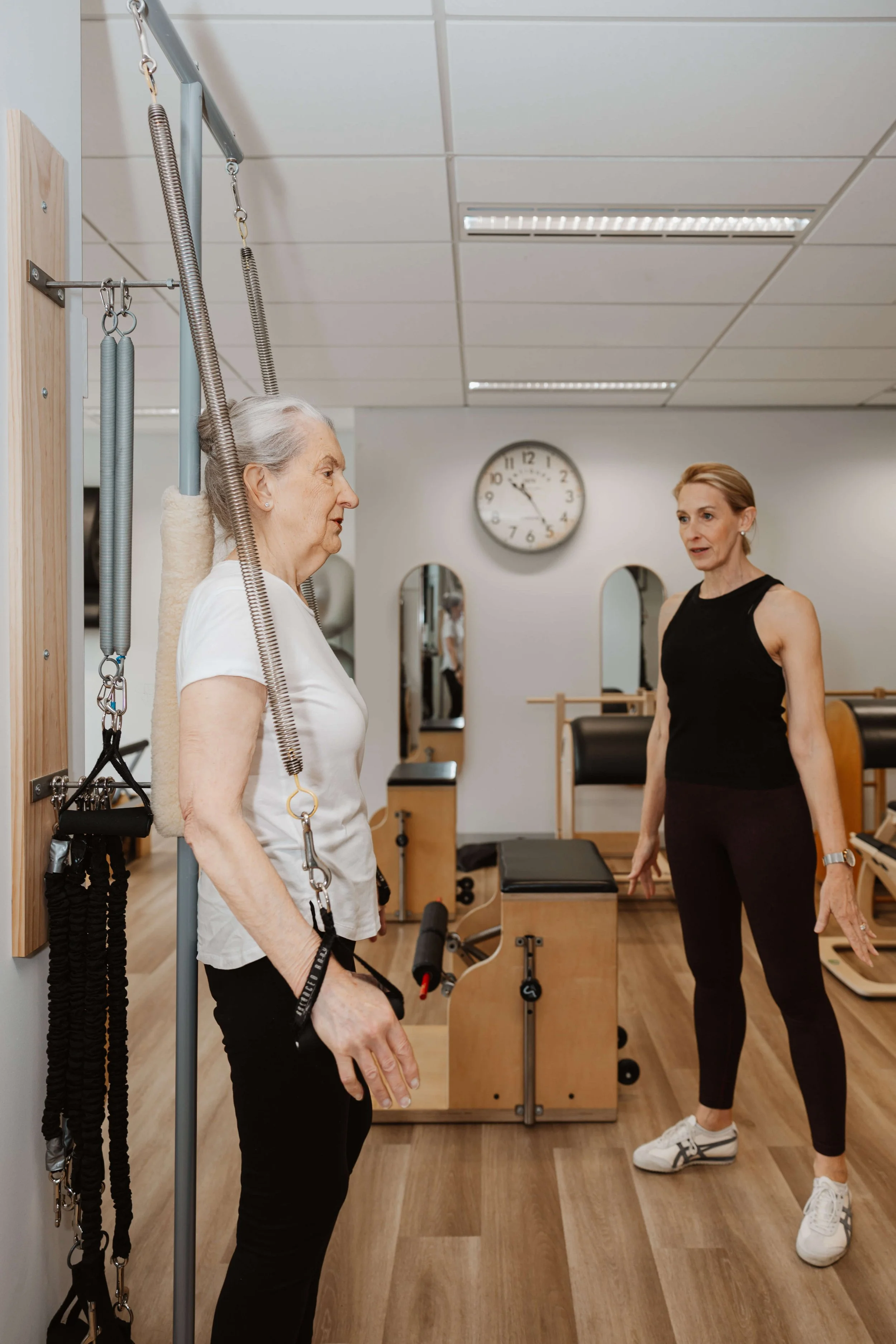 Physical therapy session with an elderly woman using a suspension aid, guided by a female therapist in a rehab clinic.