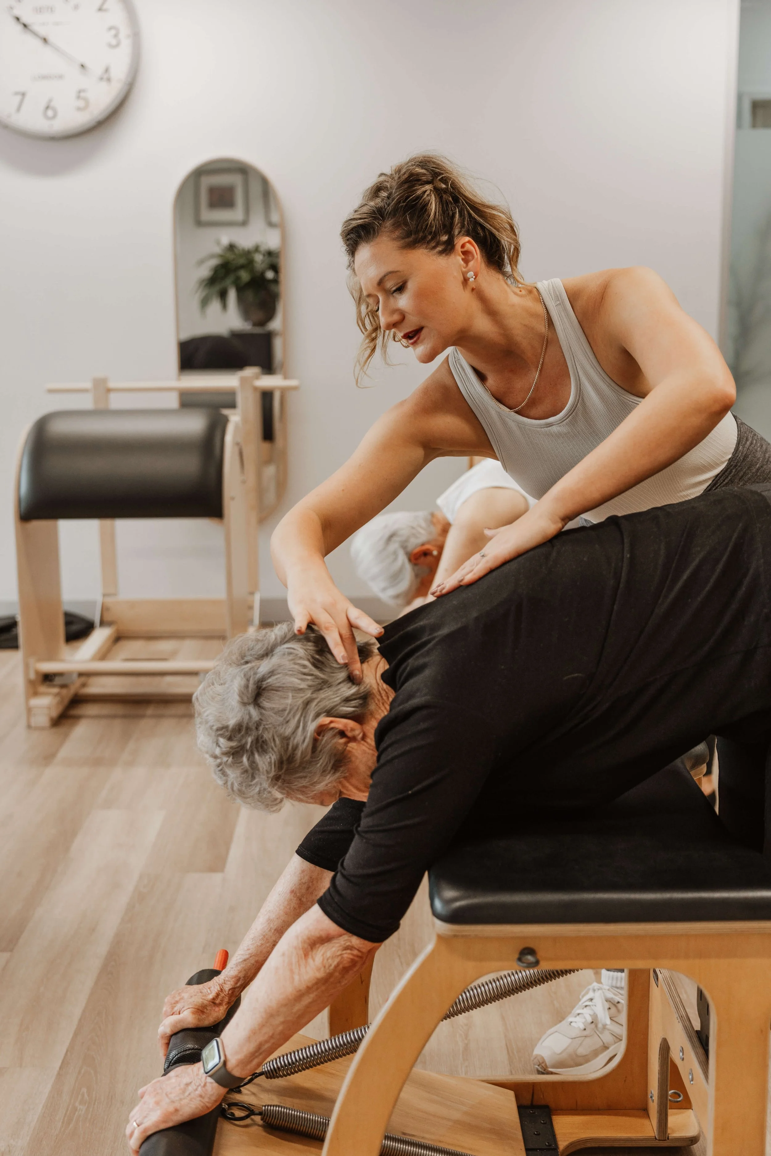 A woman assists an elderly woman with stretching exercises using a pole, in a therapy or fitness setting.