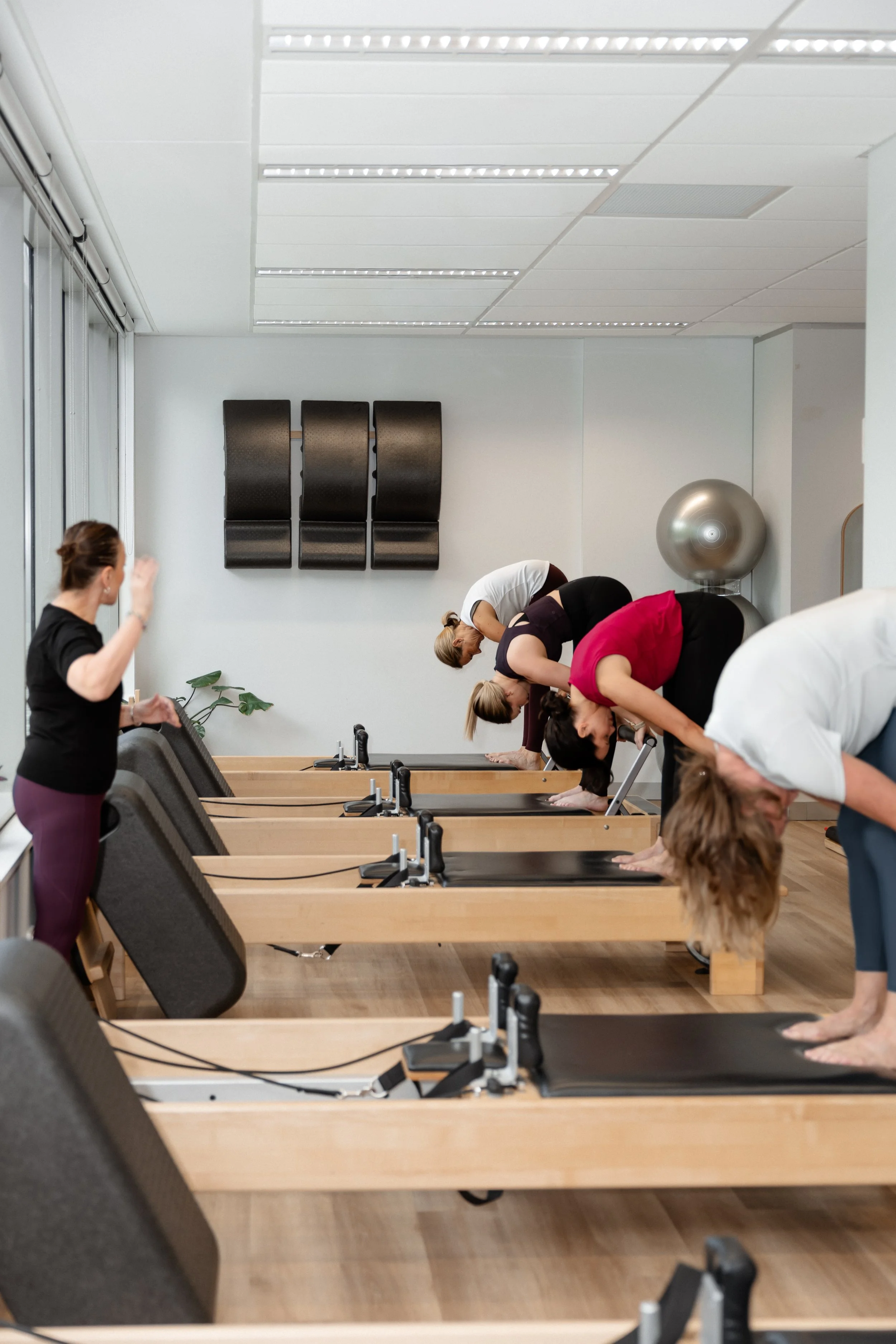 group of women practicing yoga in a wellness or fitness studio, bending forward in a yoga pose on mats, with an instructor guiding them.