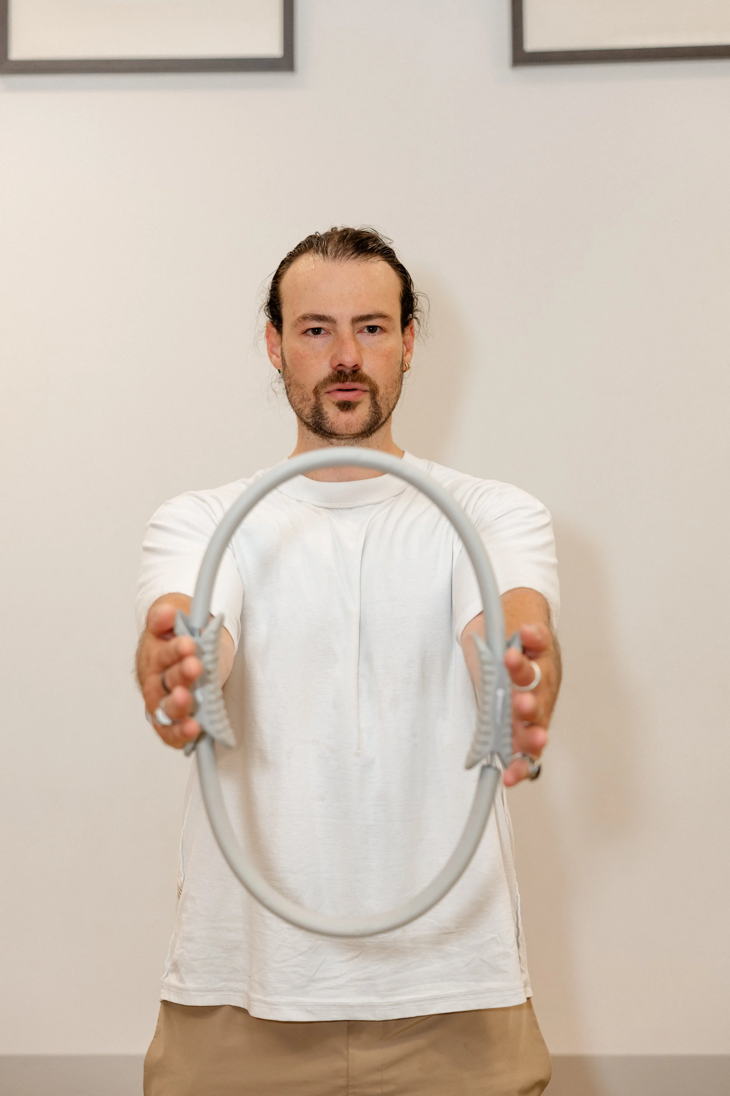 A man with dark curly hair and a beard holding a speed bag ring in front of a plain white wall.