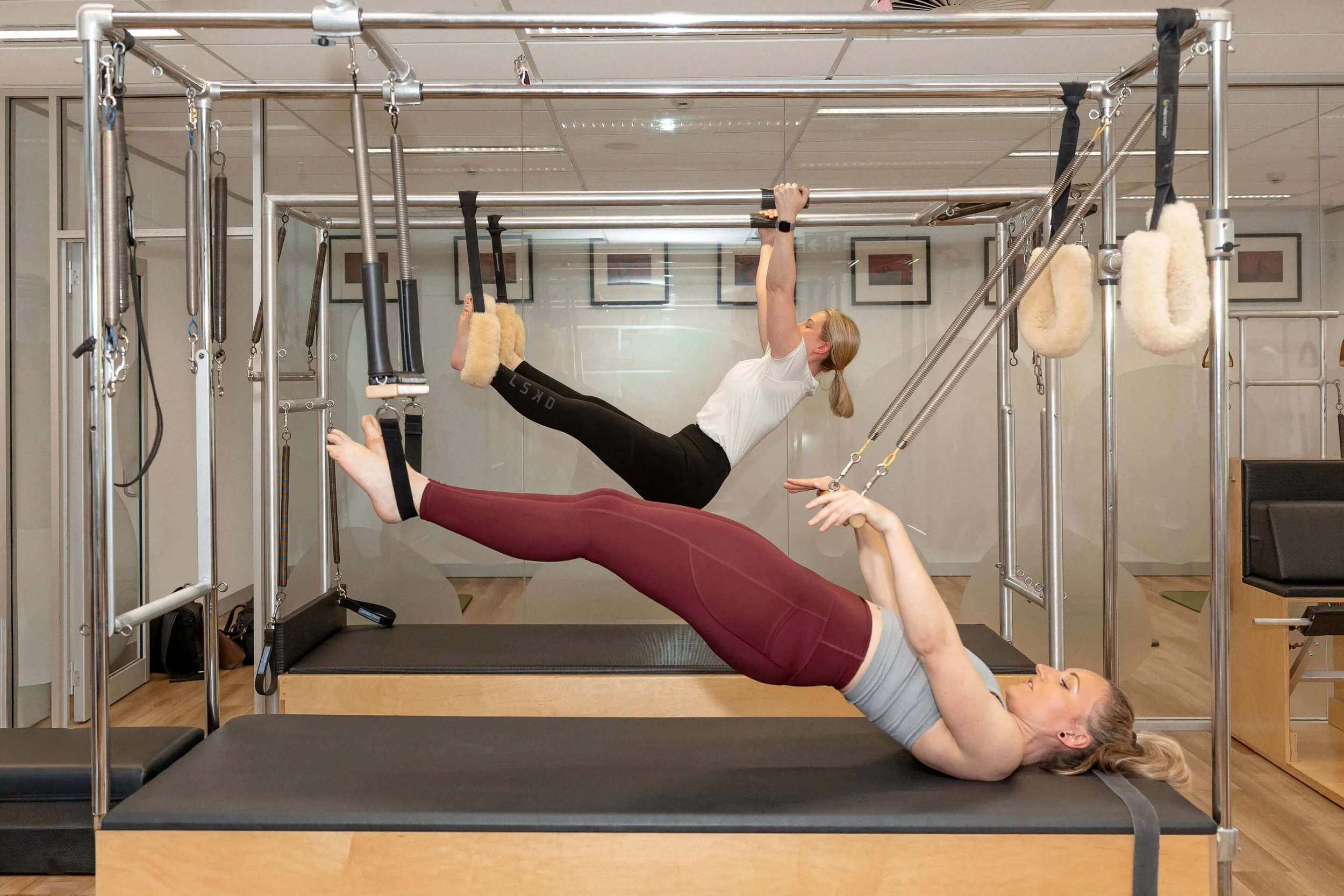 Two women exercising with suspension training equipment in a fitness studio.