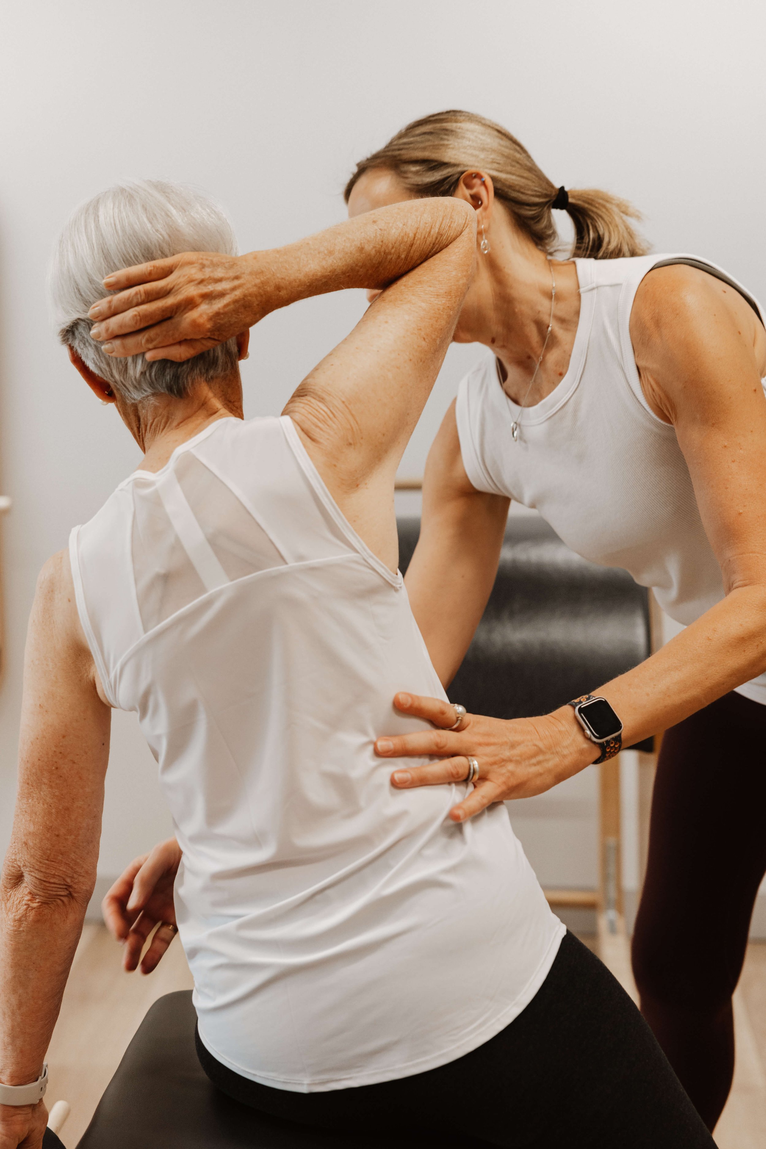 A healthcare professional assisting an elderly woman with physical therapy exercises in a clinical setting.