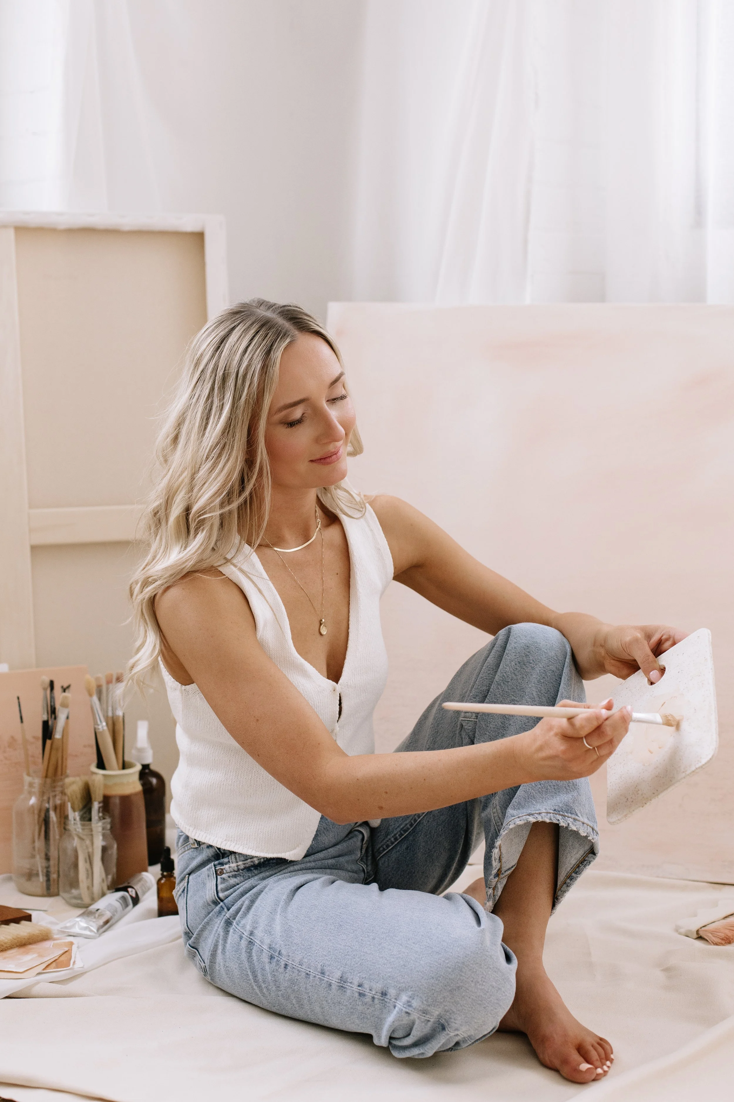 Artist painting in here studio with a handmade palette and art supplies surrounding her.