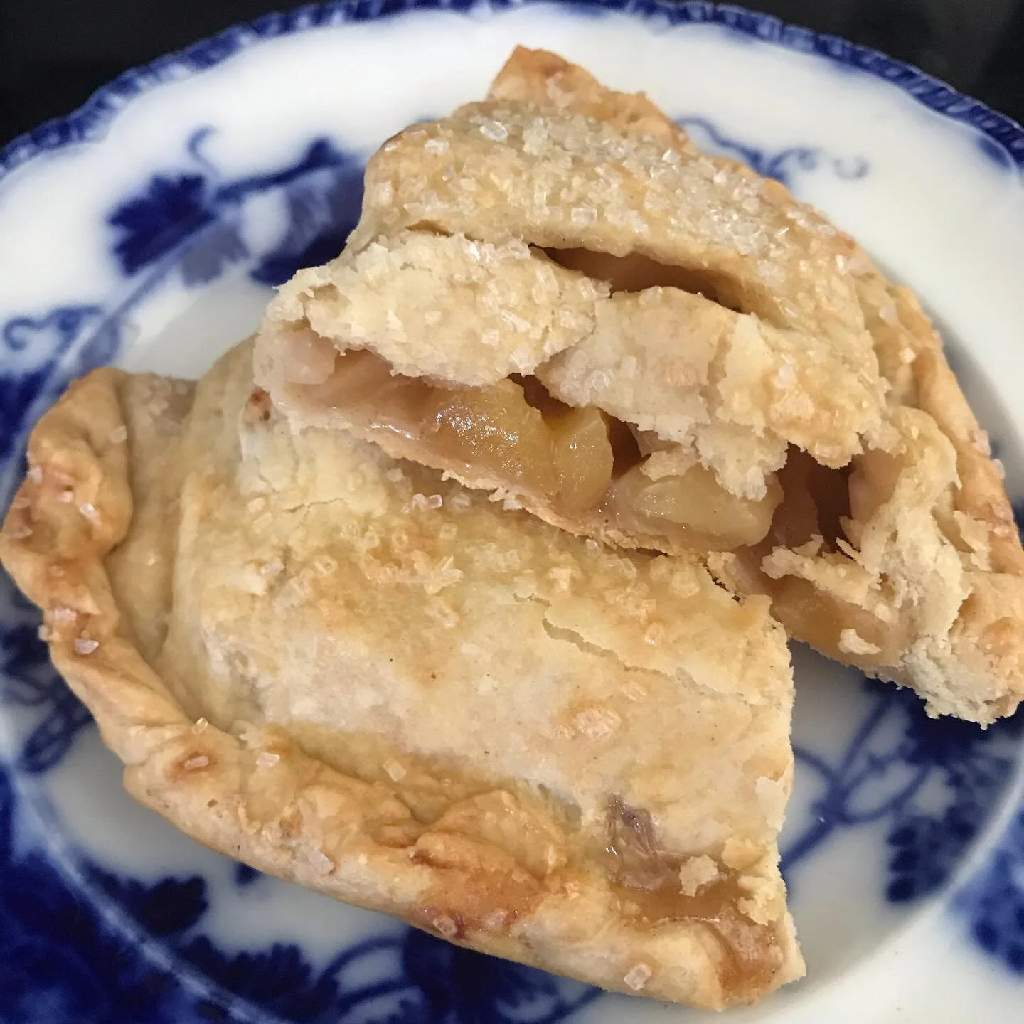 A sliced apple pie on a blue and white decorative plate, showing the apple filling inside.