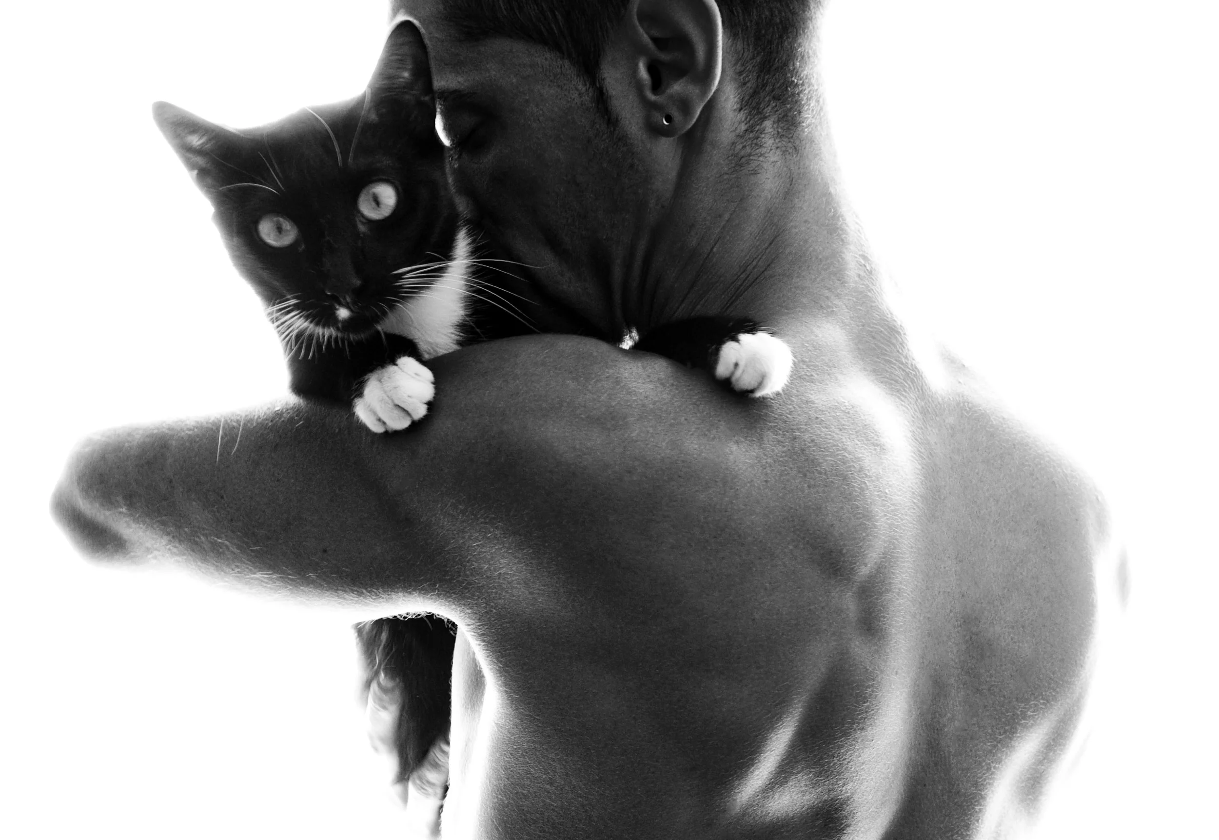 Black and white photo of a person holding a black and white cat, with the person's face partially hidden and their arm supporting the cat.