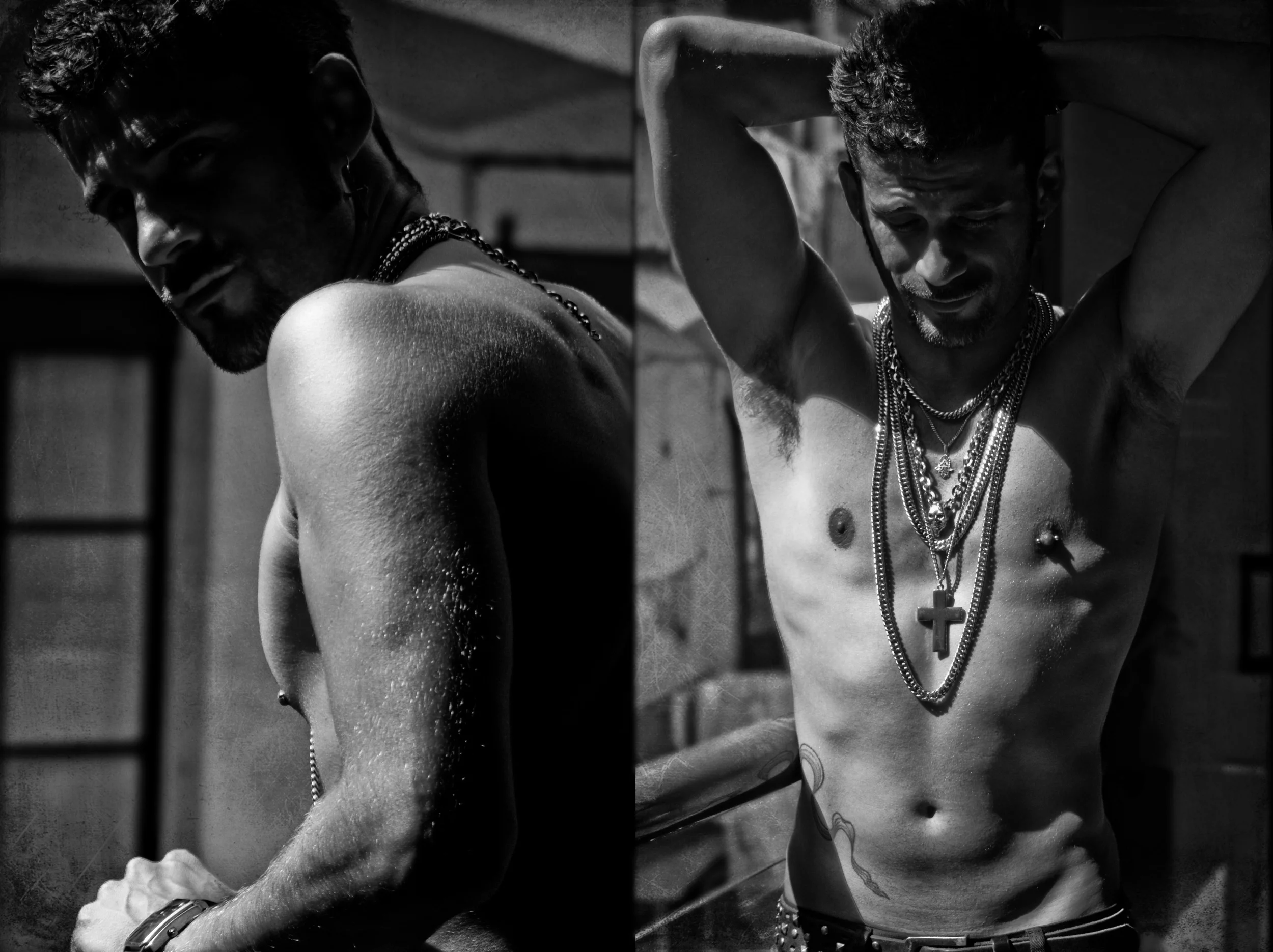 Black and white photo of two shirtless men with jewelry, both with muscular builds and tattoos, posing in a dimly lit setting, one looking at the camera and the other with their eyes closed, in a moody atmosphere.