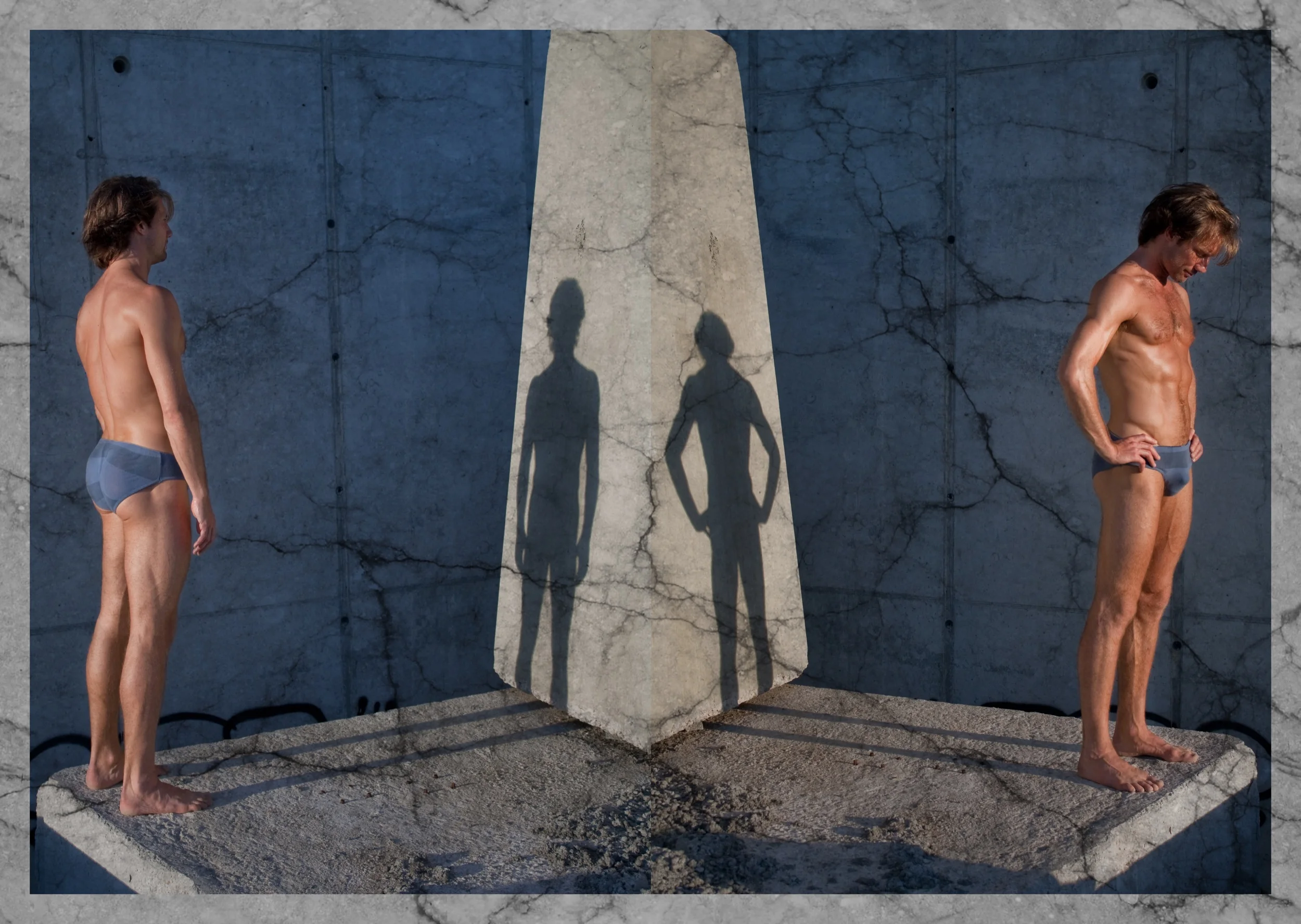 Two shirtless men in underwear standing on separate concrete blocks facing opposite directions with their shadow puppets cast on a concrete wall between them.
