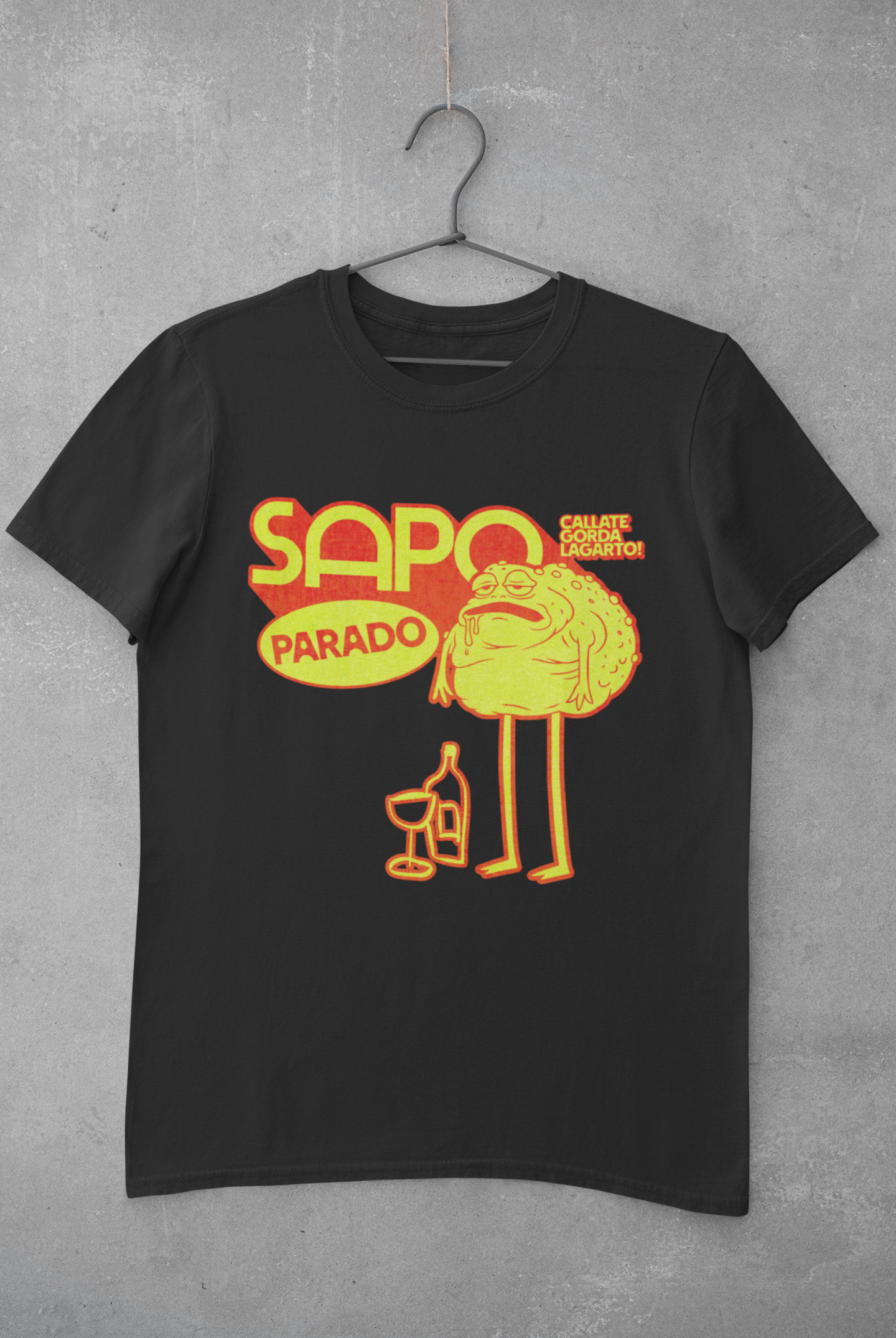Camiseta negra con un dibujo de una fruta con cara y piernas, acompañada de una copa y una botella, y texto en amarillo y rojo que dice 'SAPO PARADO' y 'CALLATE GORDA LÁRGATO!' sobre una anécdota del comediante y streamer argentino Martin Cirio