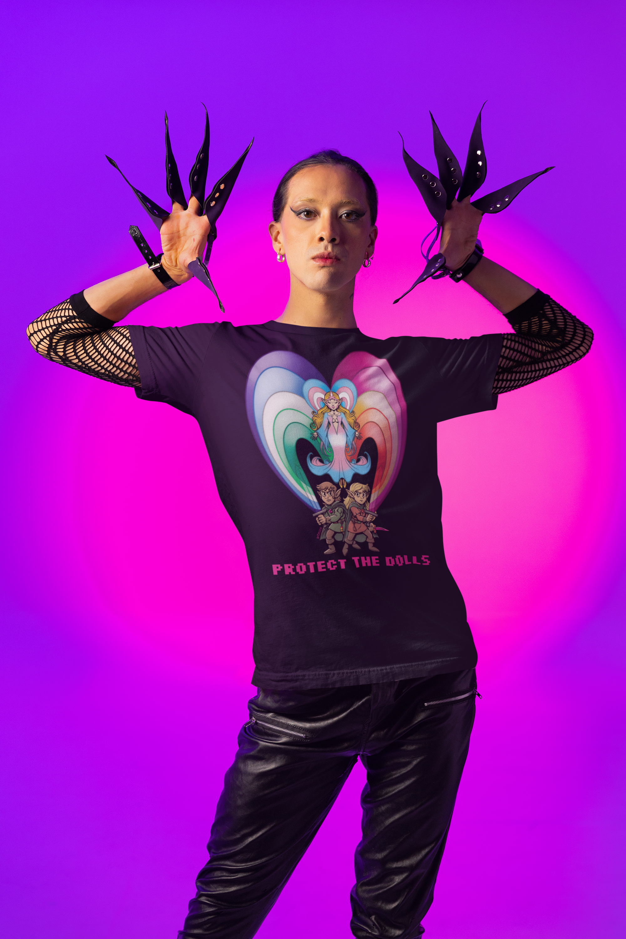 Una persona con maquillaje atrevido y ropa negra, lleva guantes con forma de cuchillas, en un fondo de luces moradas y rosas. Viste camiseta con ilustración de personajes y la frase 'Protect the Dolls'.