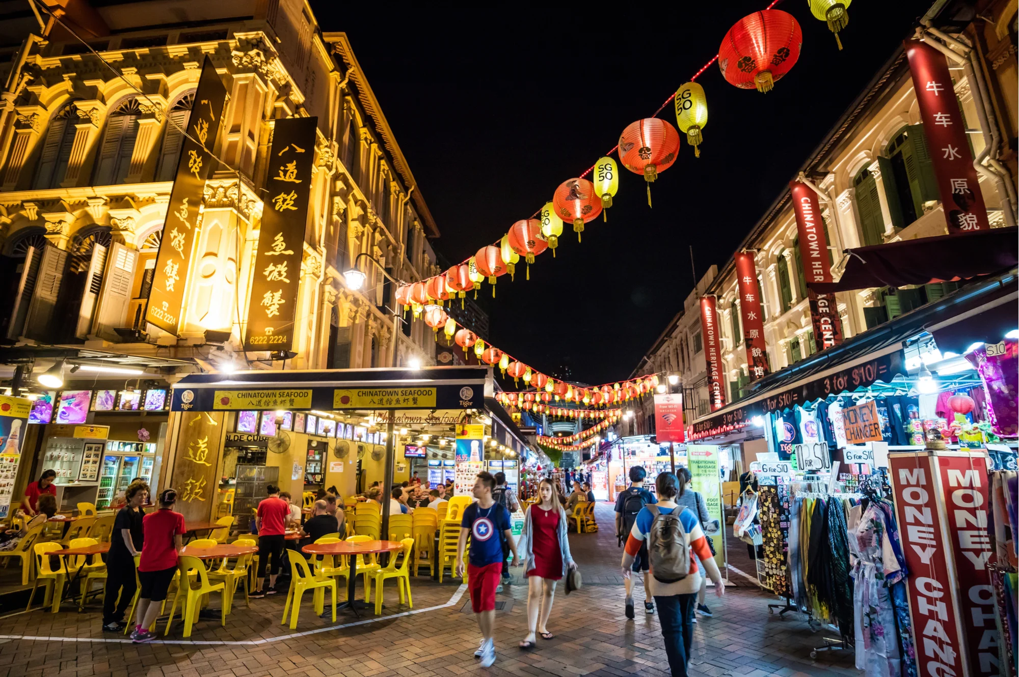 Chinatown at nighttime with lanterns criss-crossing a street filled with shoppers and restaurant-goers