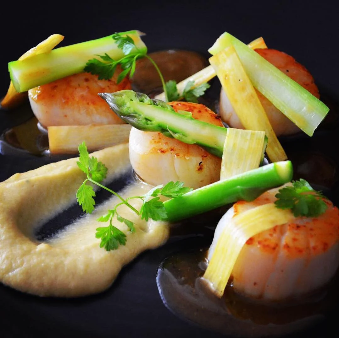 Seared scallops with asparagus and burnt tosazu butter on a black plate at Cocotte Dining French Restaurant