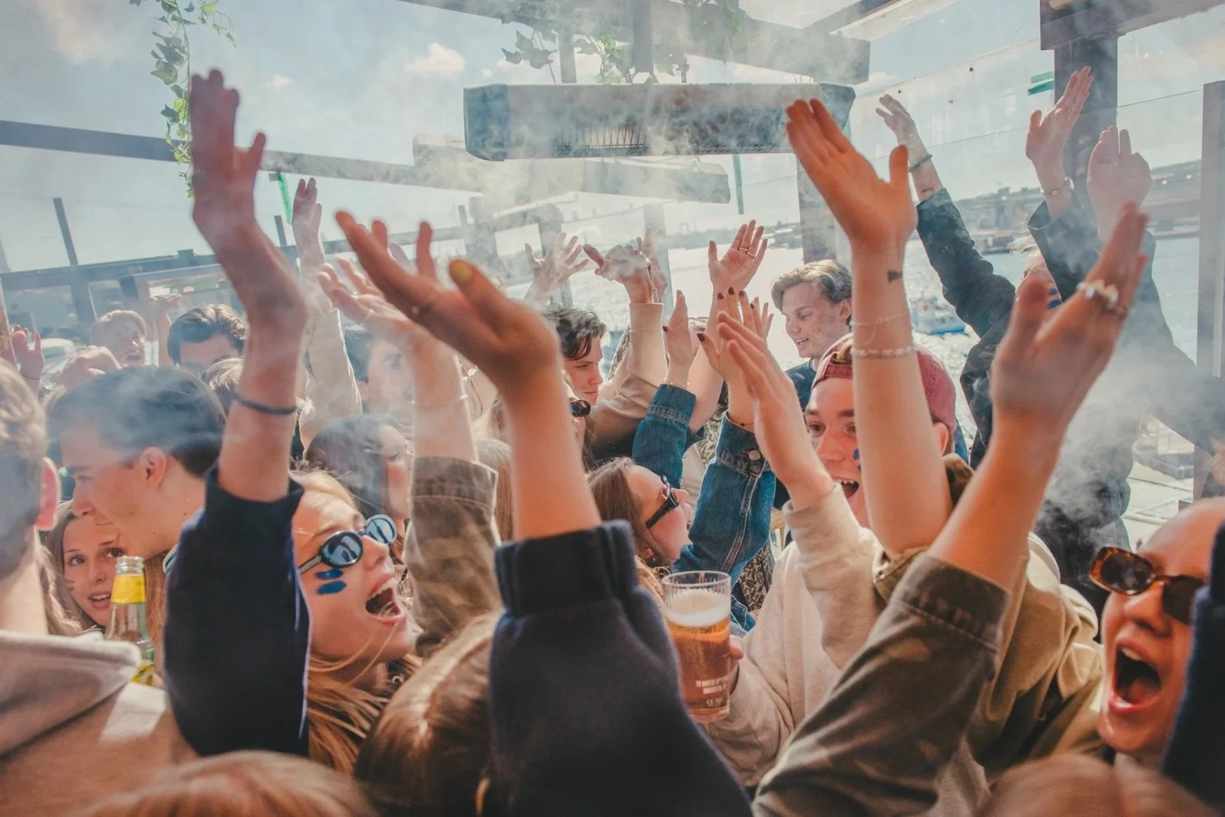 En grupp människor som dansar och har roligt inom en lokal, med utsikt över en sjö eller vattendrag utanför stora fönster, på en fest eller social tillställning.