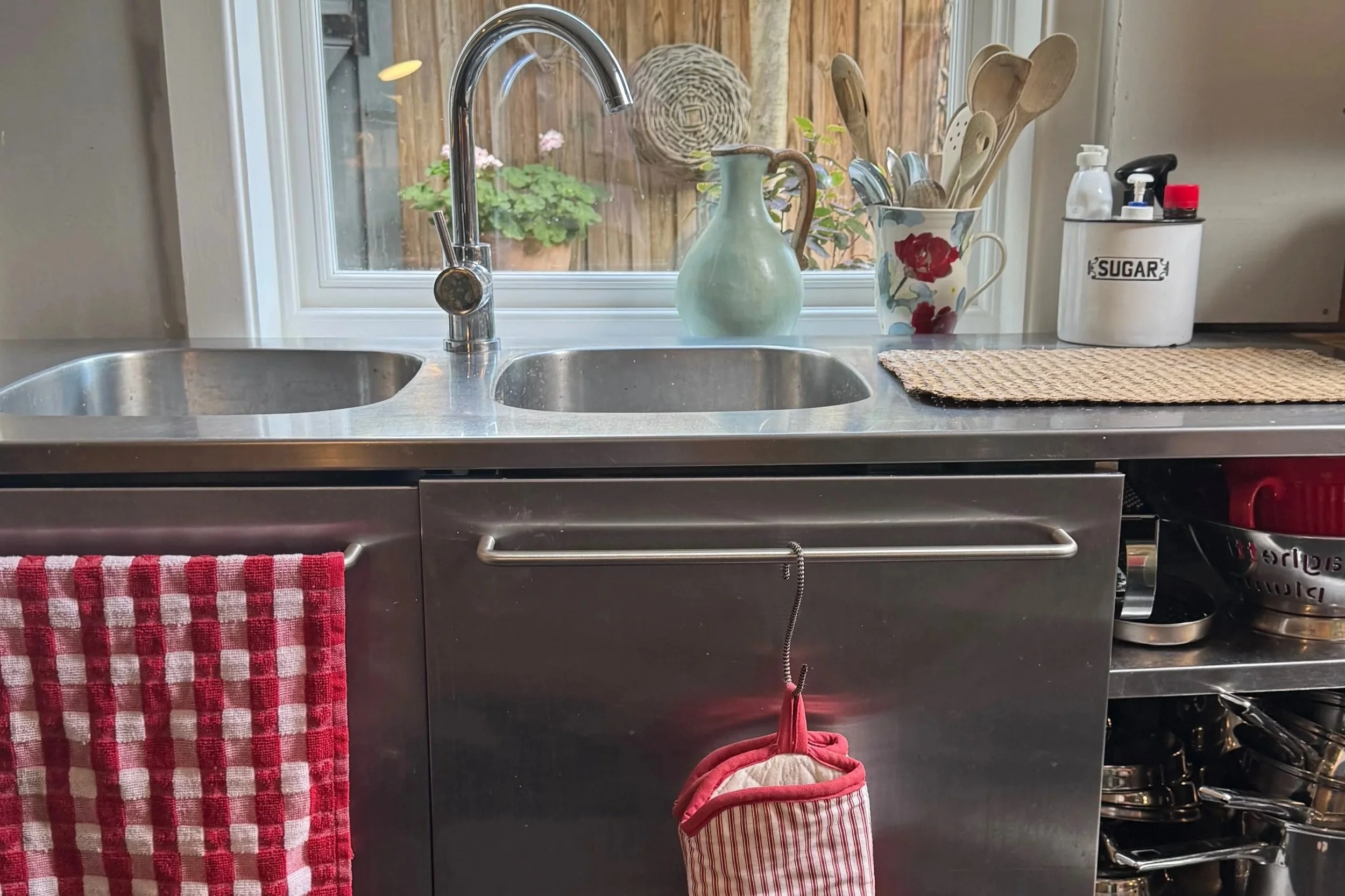 Stainless steel double kitchen sinks with red tea towel and oven gloves in front of large window