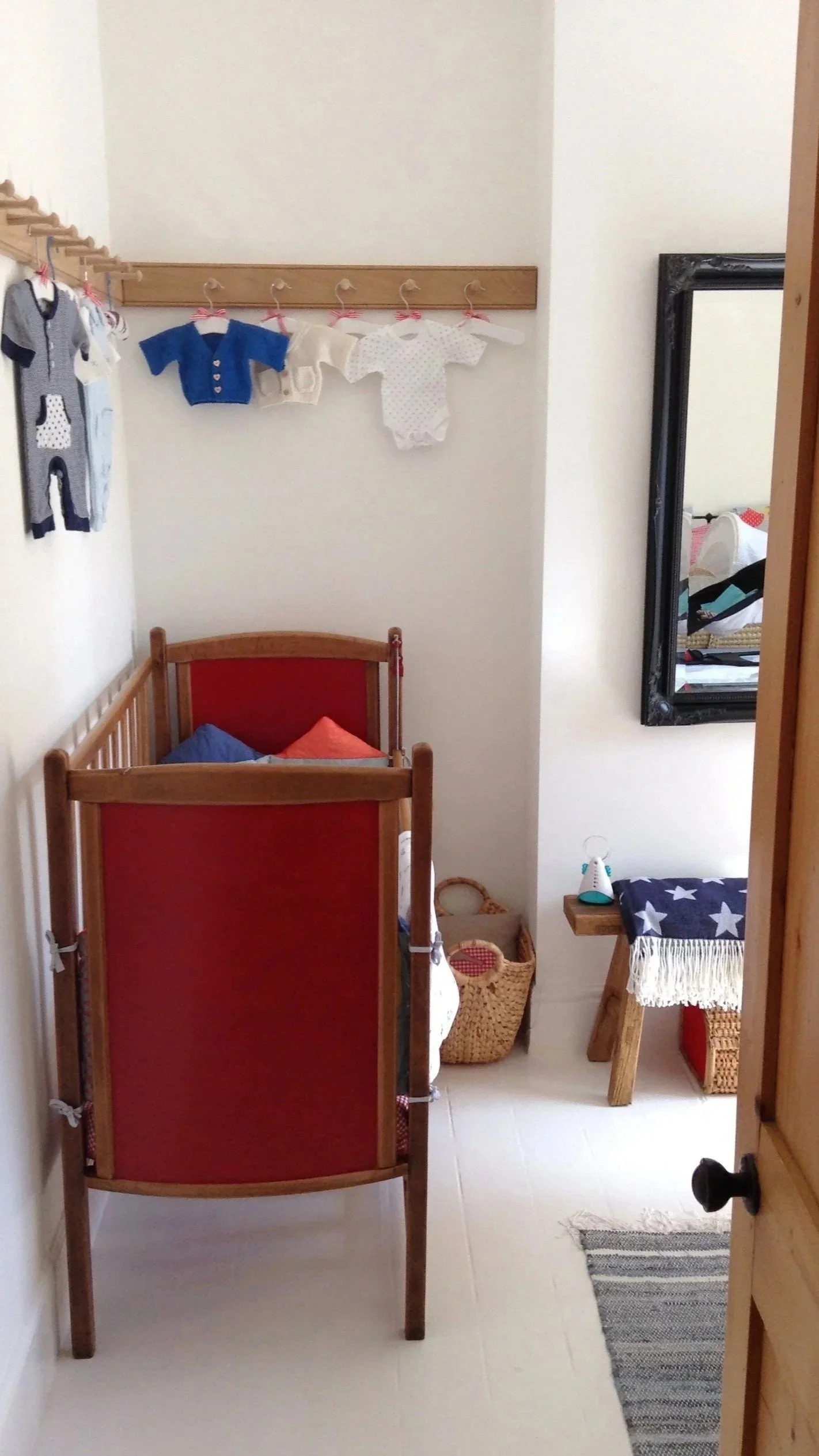 View through door into white room with red painted cot and peg rail hanging on wall