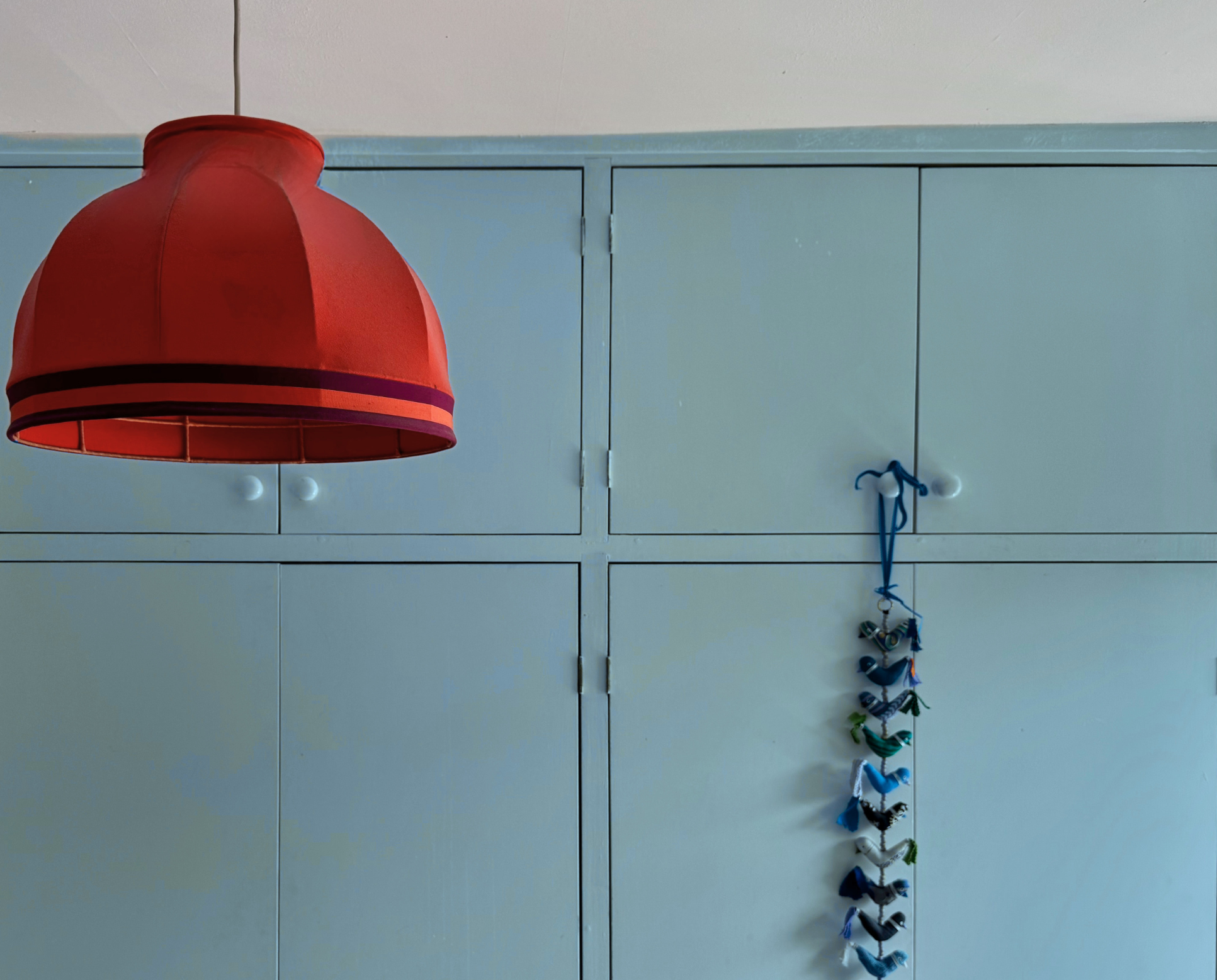 A red hanging lampshade and a string of colorful scrunchies hanging on a hook on a light blue cabinet.