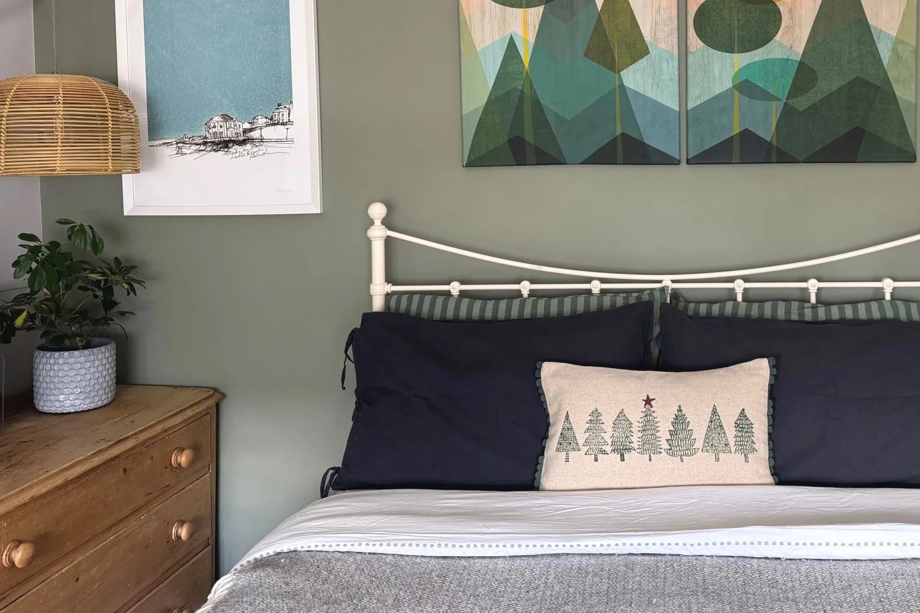 View of bed with grey and green bedding and wooden chest of drawers with pictures on the wall