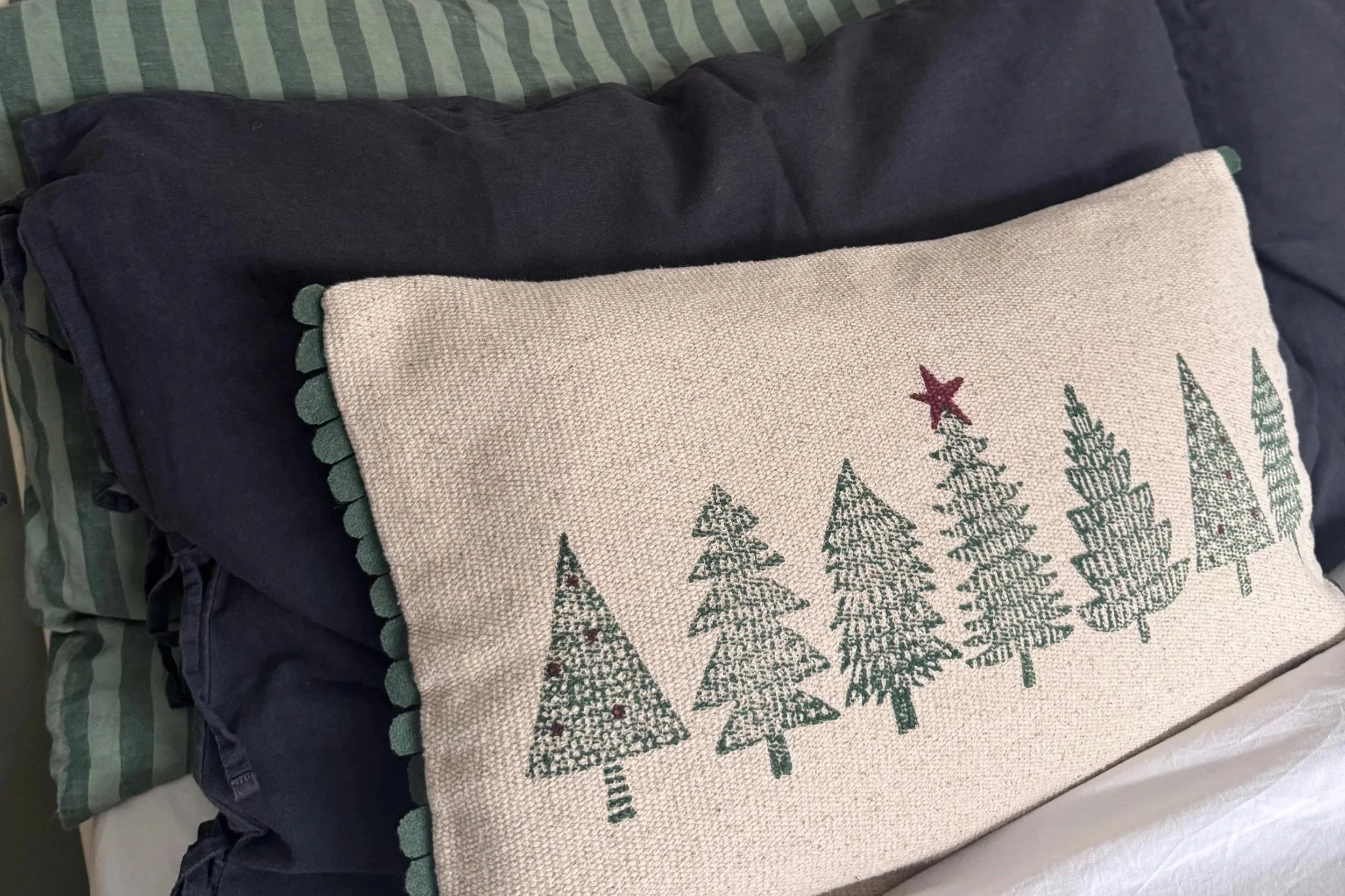 three pillows and cushions in navy, green stripe and cushion with a Christmas tree pattern