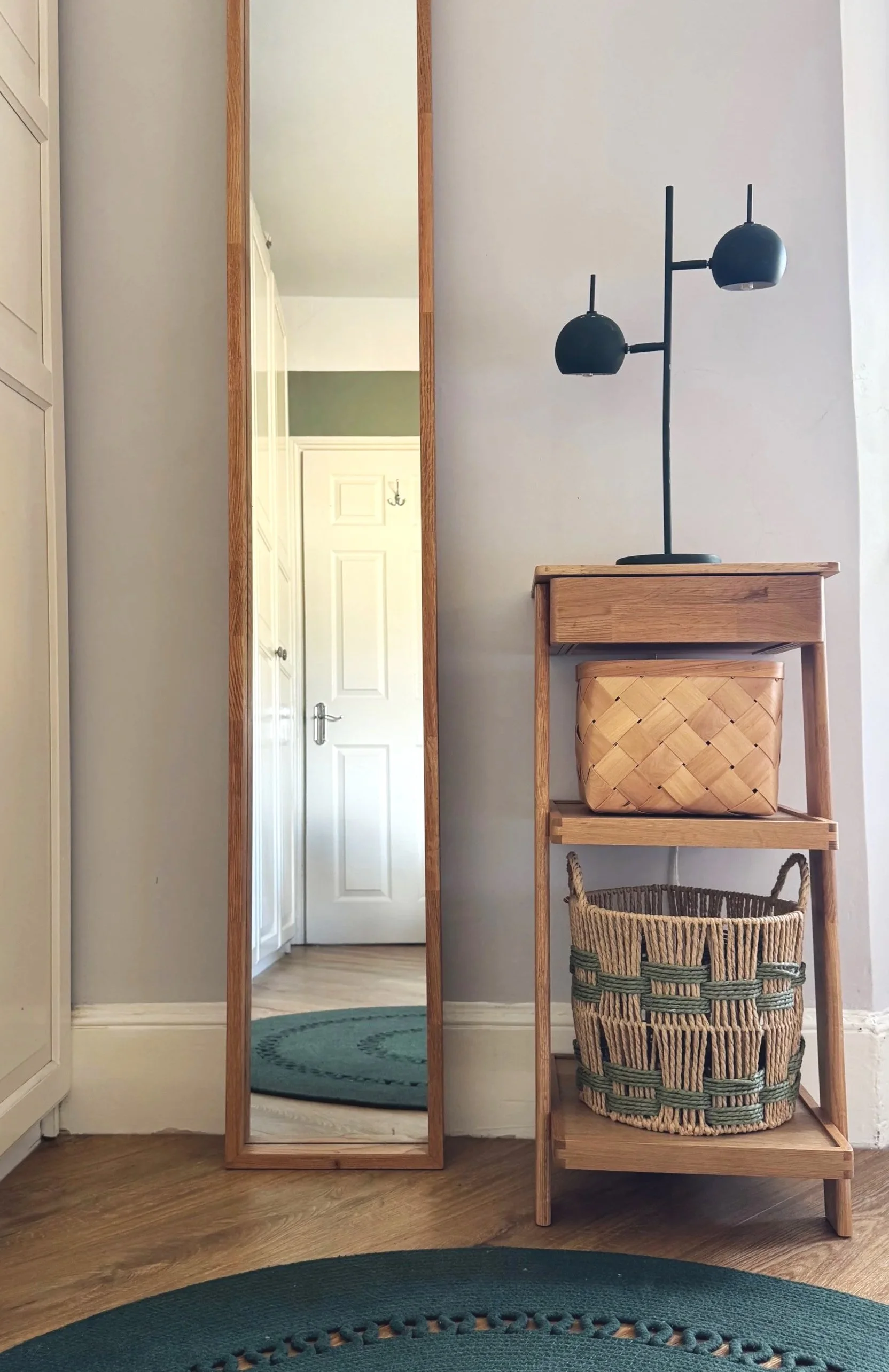 Long mirror and small wooden ladder style table with green spotlight and green circular rug