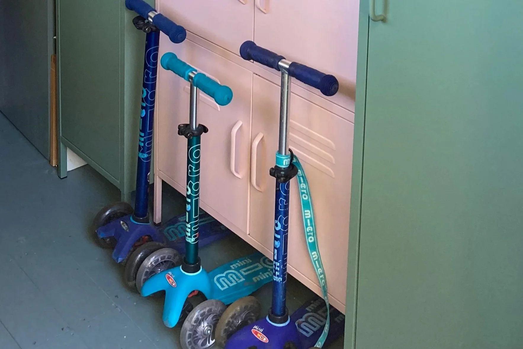 Three children scooters next to pink and green metal lockers