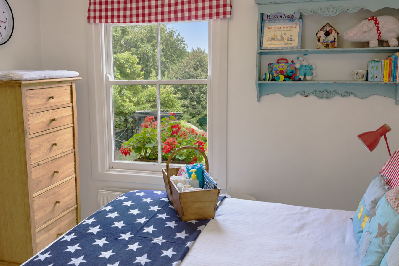 Double bed in nursery with blue and white starred blanket and oak chest of drawers near window