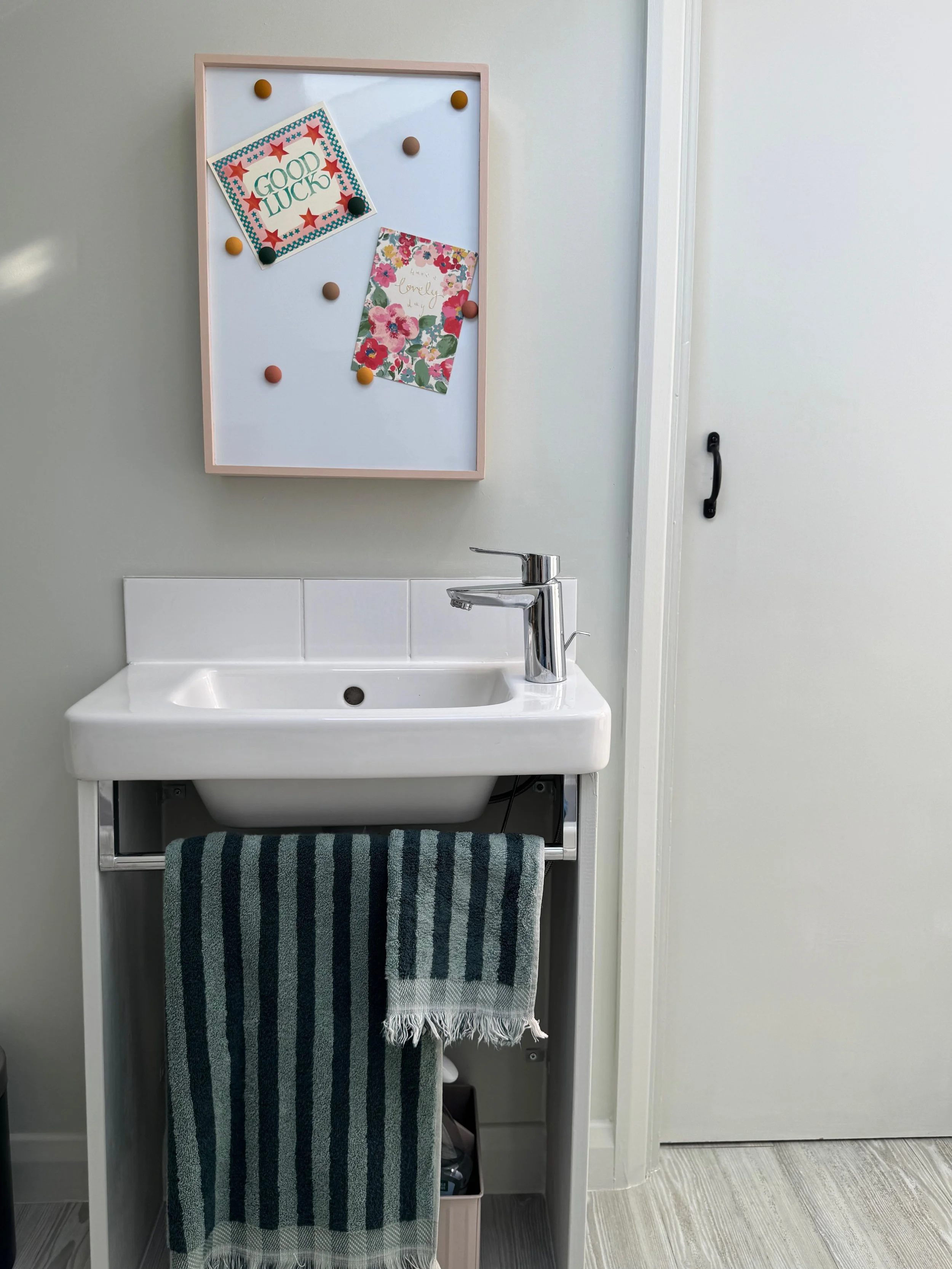 Small bathroom sink with green striped towels and pale green walls and pink cupboard over sink