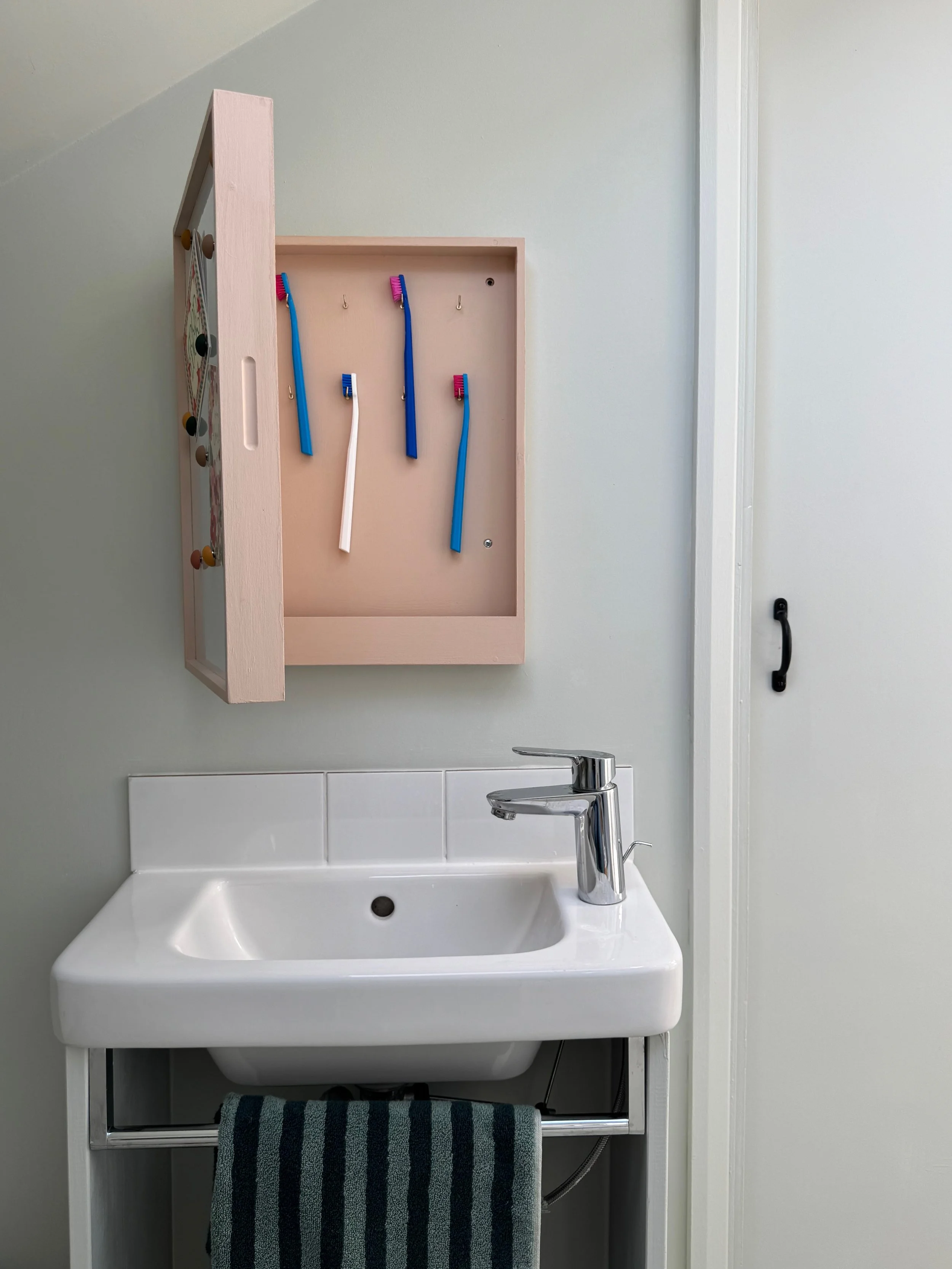Bathroom vanity with a white sink, chrome faucet, small mirror, and a towel rack with a striped towel below the sink.