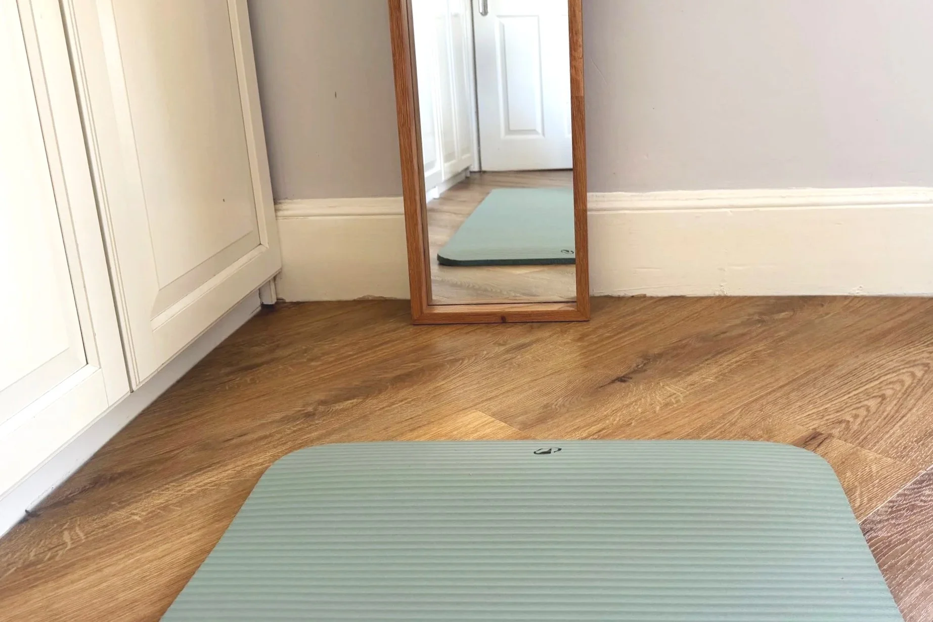 Green exercise mat on wooden floor and bottom of long mirror