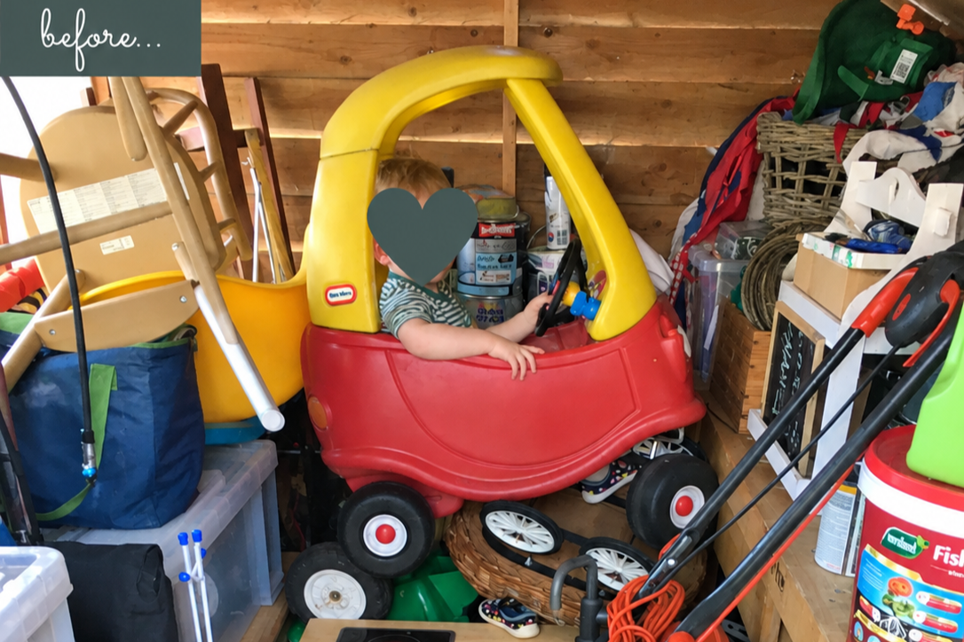 Child sitting with face hidden sitting in red and yellow toy car in a very messy shed