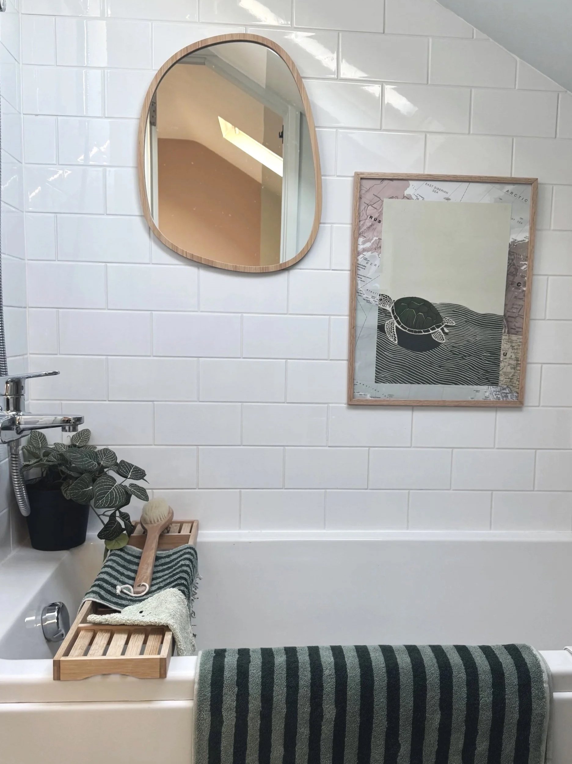 View of white tiled wall of bathroom with mirror and picture hanging on wall
