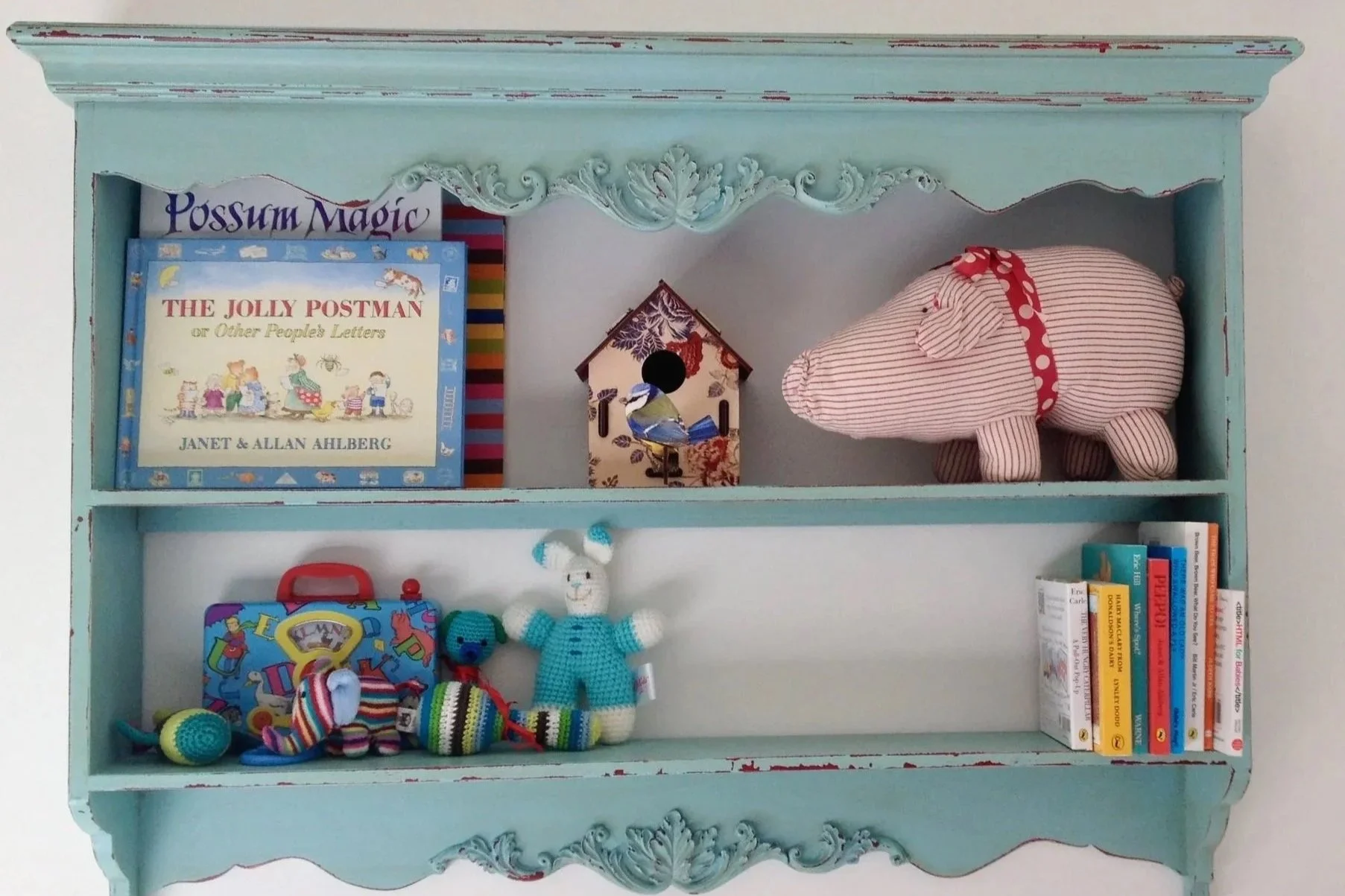 Book shelf painting blue with babies books, toys and a soft toy pig