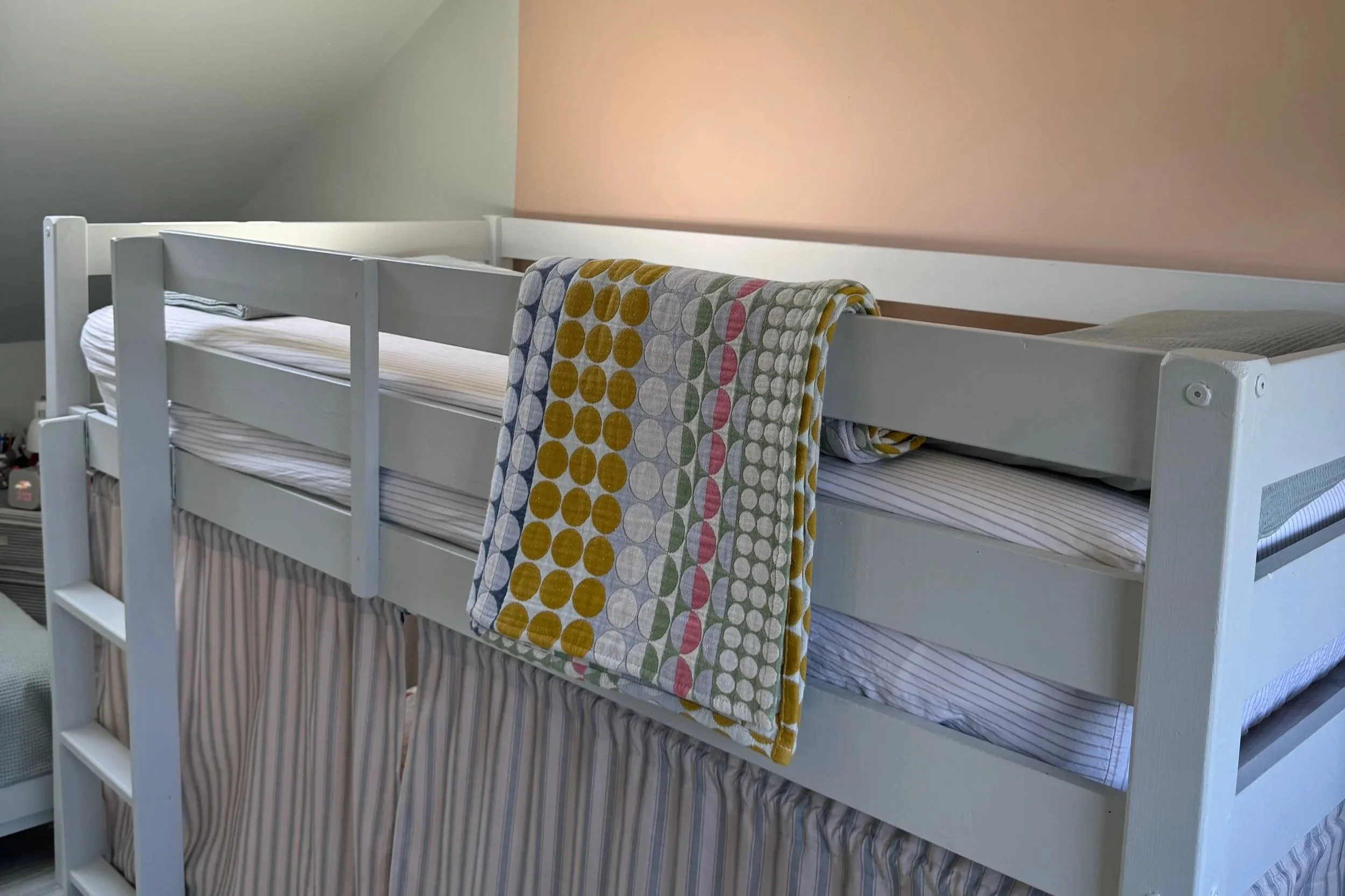 Top bunk of bunk beds painted pale green with patterned blanket and pale pink and green walls