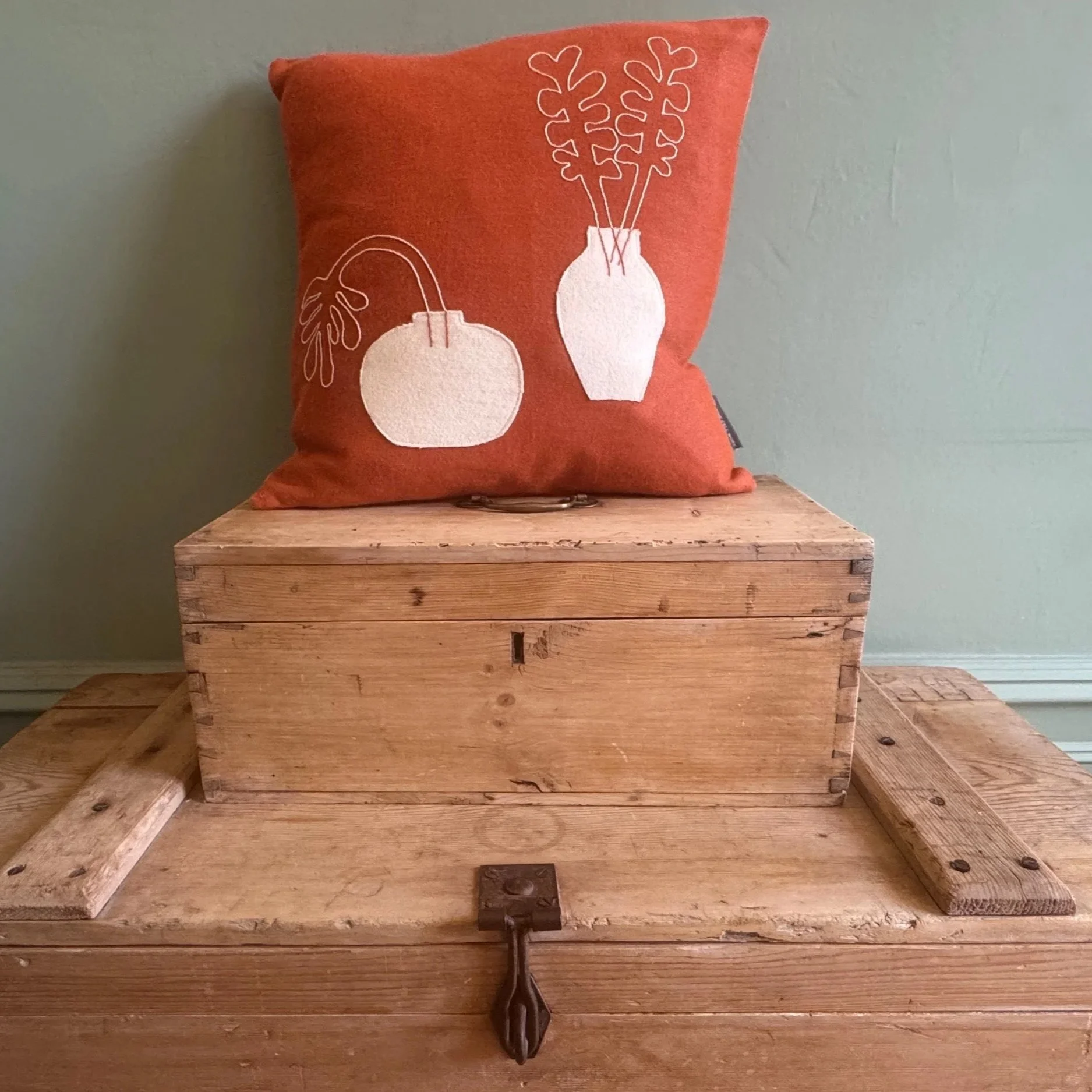 A red decorative pillow featuring minimalist white line drawings of vases with botanical motifs, placed on a wooden surface against a green wall.