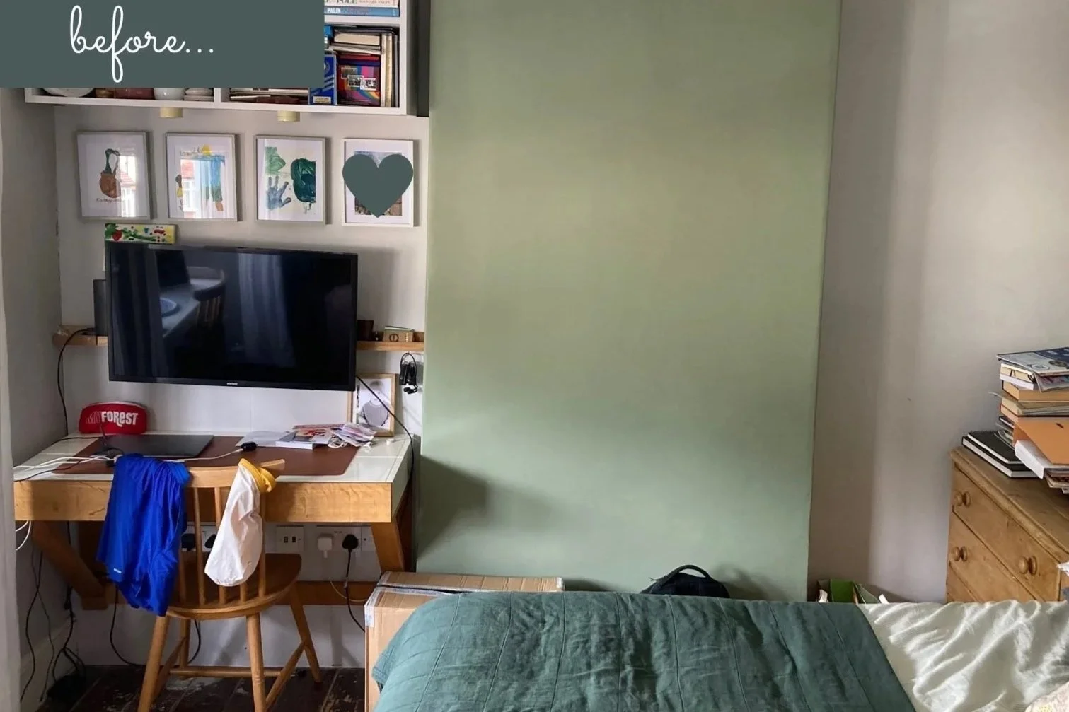 View of messy desk with black screen and shelves and green feature wall